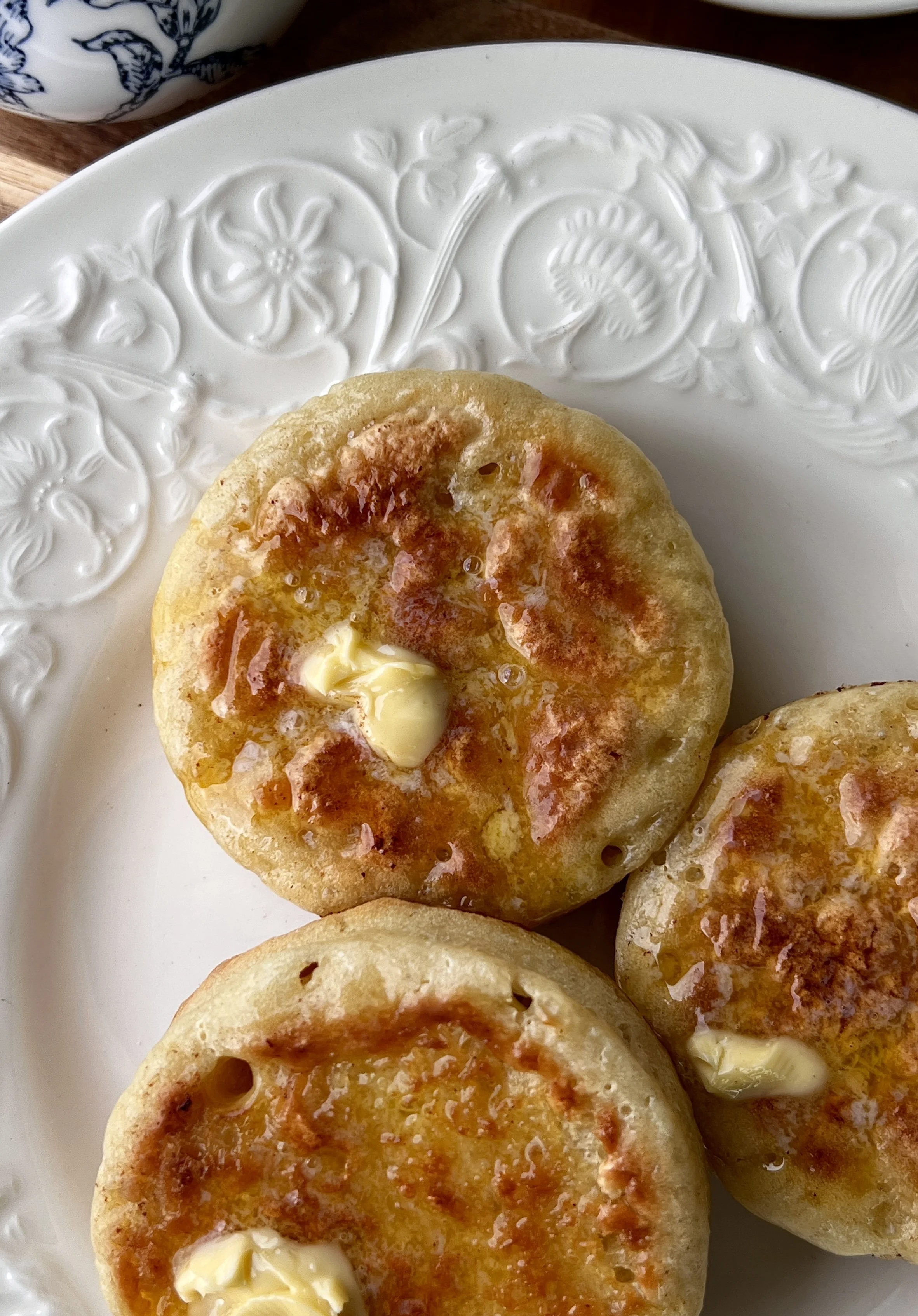 Close-up of a soft and fluffy homemade crumpet with signature holes filled with butter and bright blueberry compote.