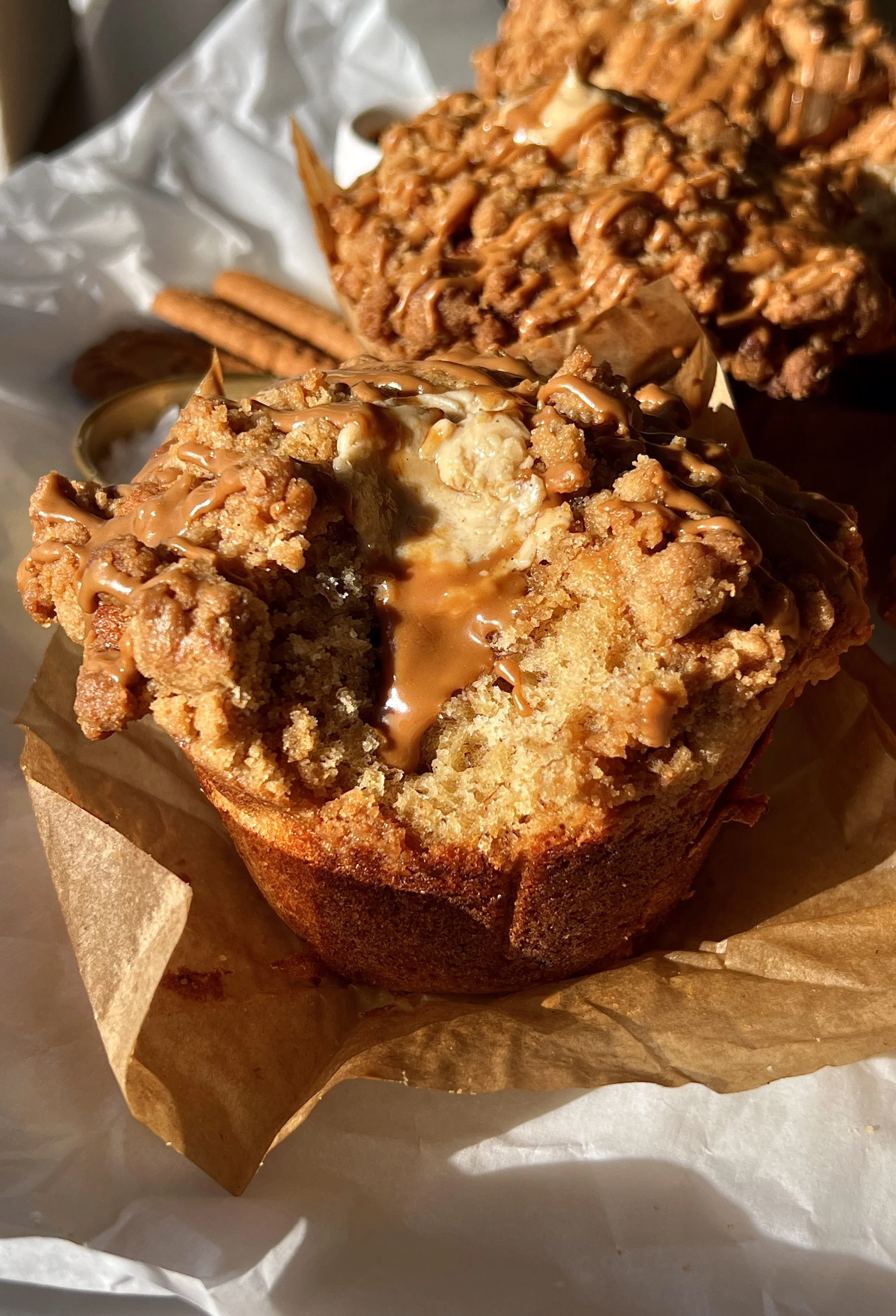 Bakery-style banana Biscoff muffin with a bite taken out showing the soft fluffy tender banana crumb with a rich Biscoff cream cheese filling and Biscoff cookie butter melting inside with a golden Biscoff streusel topping.