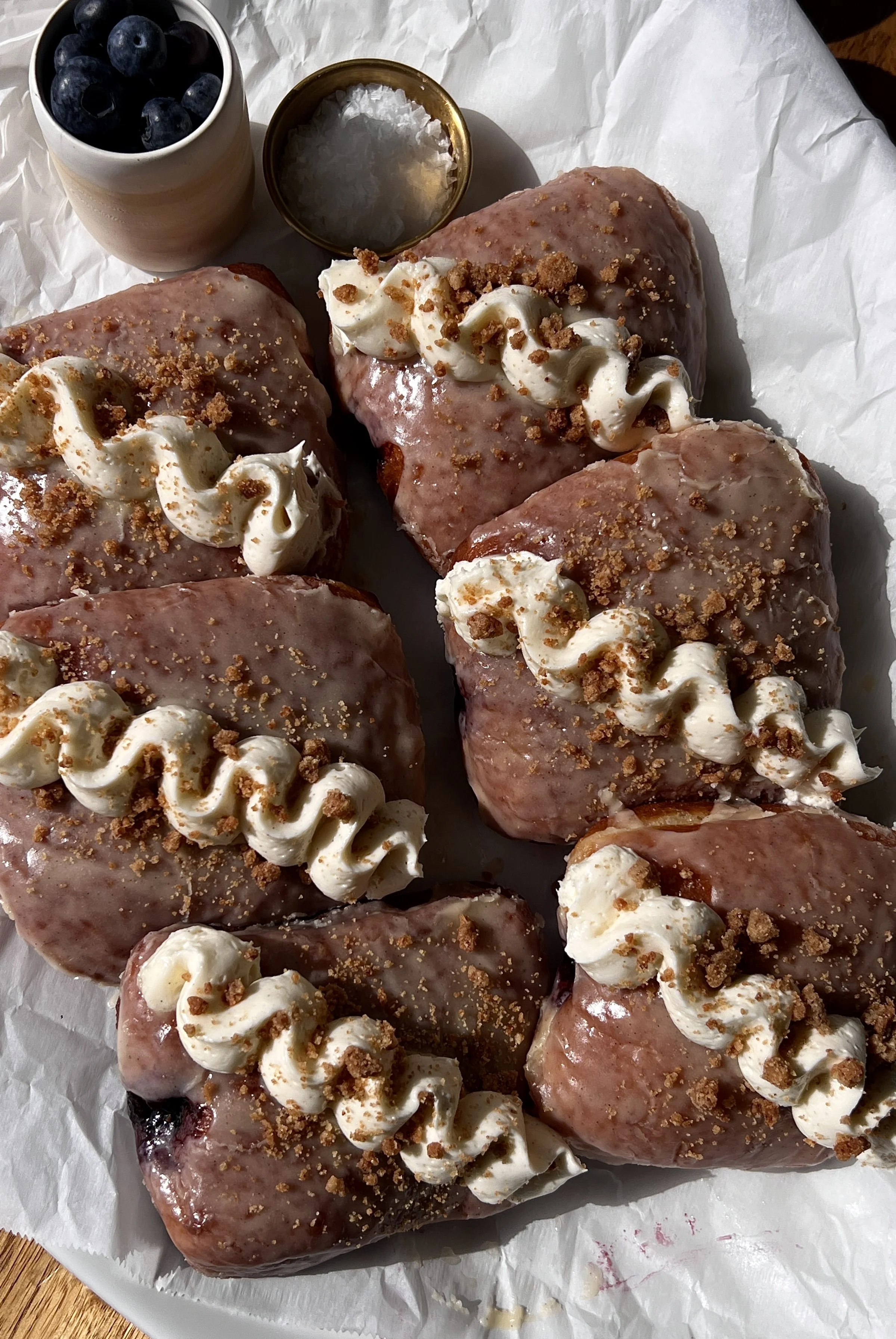 Blueberry pie donut bars coated in a silky vanilla bean glaze topped with whipped buttercream and shortbread crumbles served warm with a hot cup of coffee.
