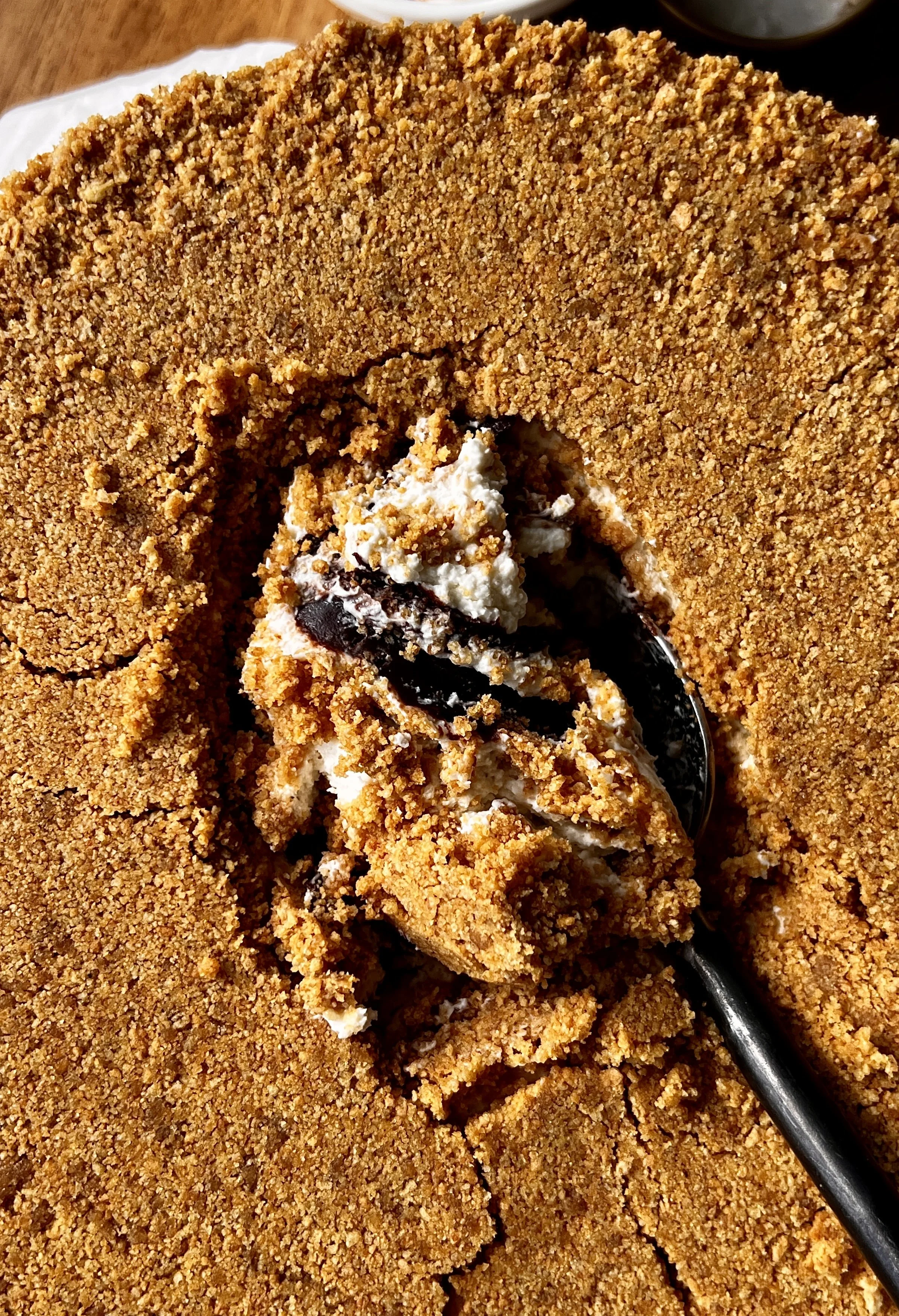 Upside down s'mores cheesecake being smashed into with a spoon revealing the rich and creamy toasted marshmallow cheesecake filling and thick hot fudge sauce inside.