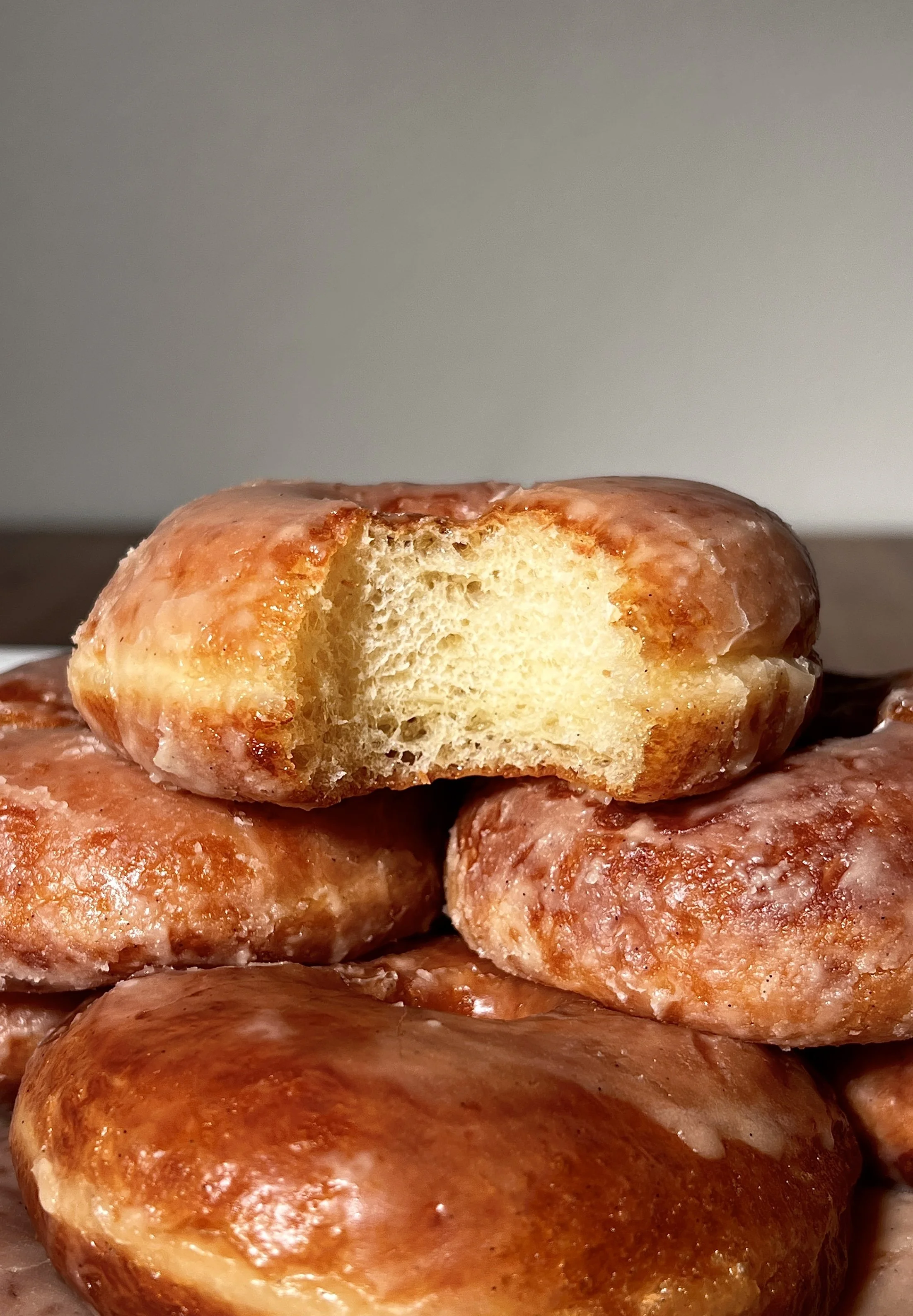 Classic vanilla bean glazed donuts served warm, showing a golden exterior and soft, pillowy interior, coated in a crackly vanilla bean glaze with coffee on the side.