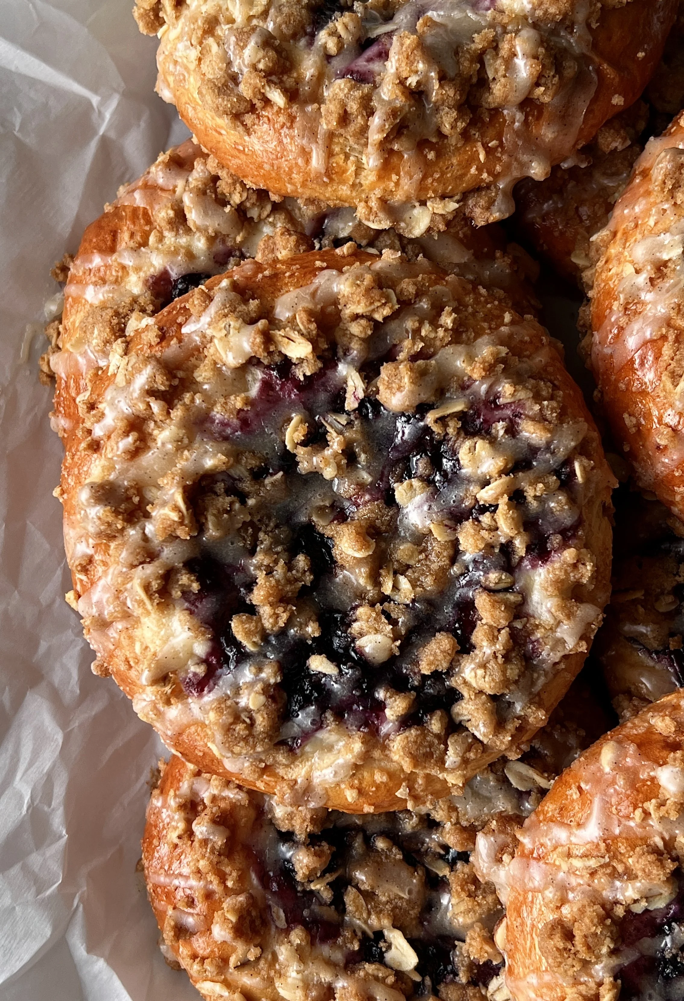 Close-up of a soft and pillowy blueberry cheesecake streusel bun with a rich and tangy cheesecake filling, homemade jammy blueberry compote, and golden oat streusel throughout.