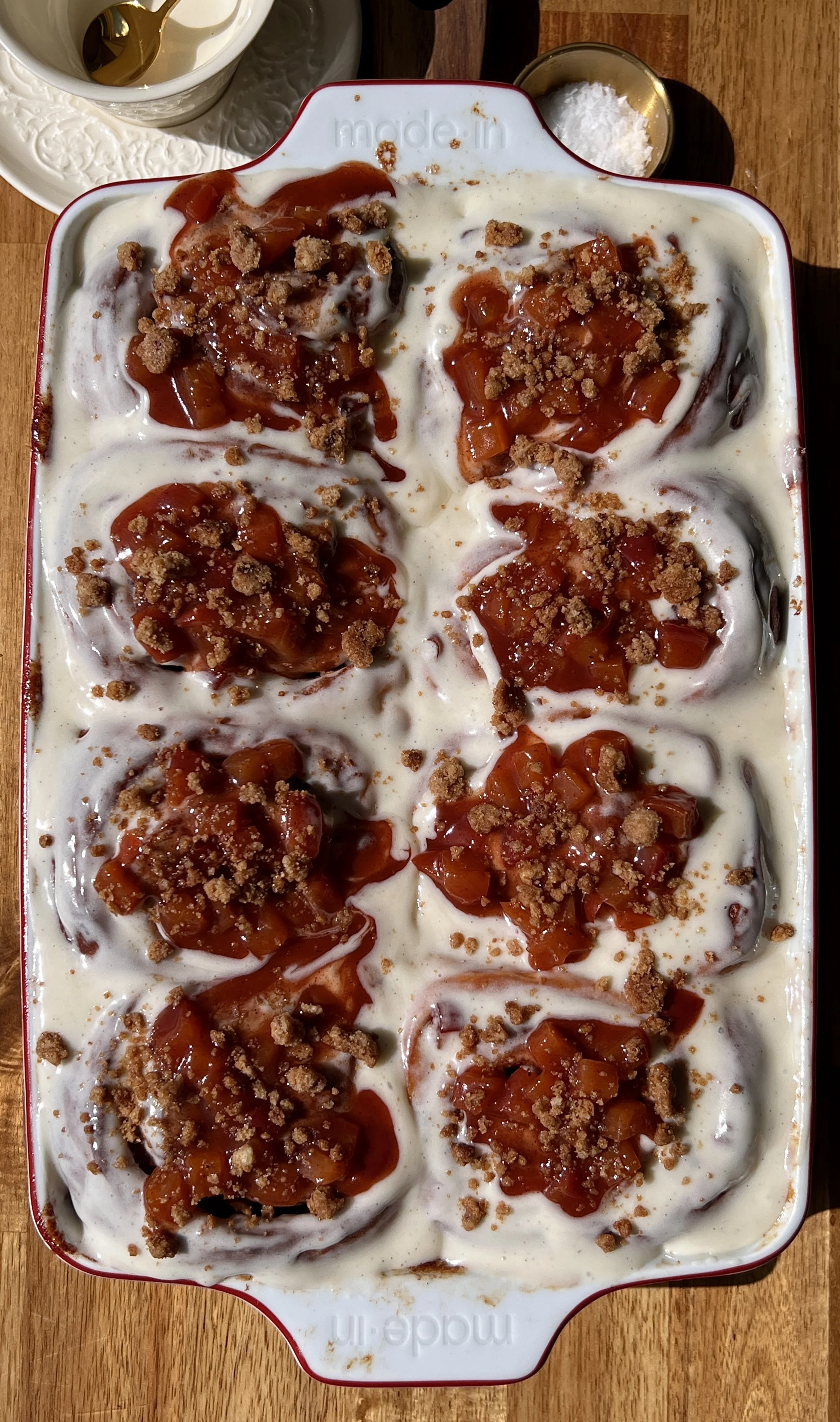 Pan of golden peach cobbler cinnamon rolls with sticky caramelized edges topped with smooth cream cheese frosting melting into every swirl.