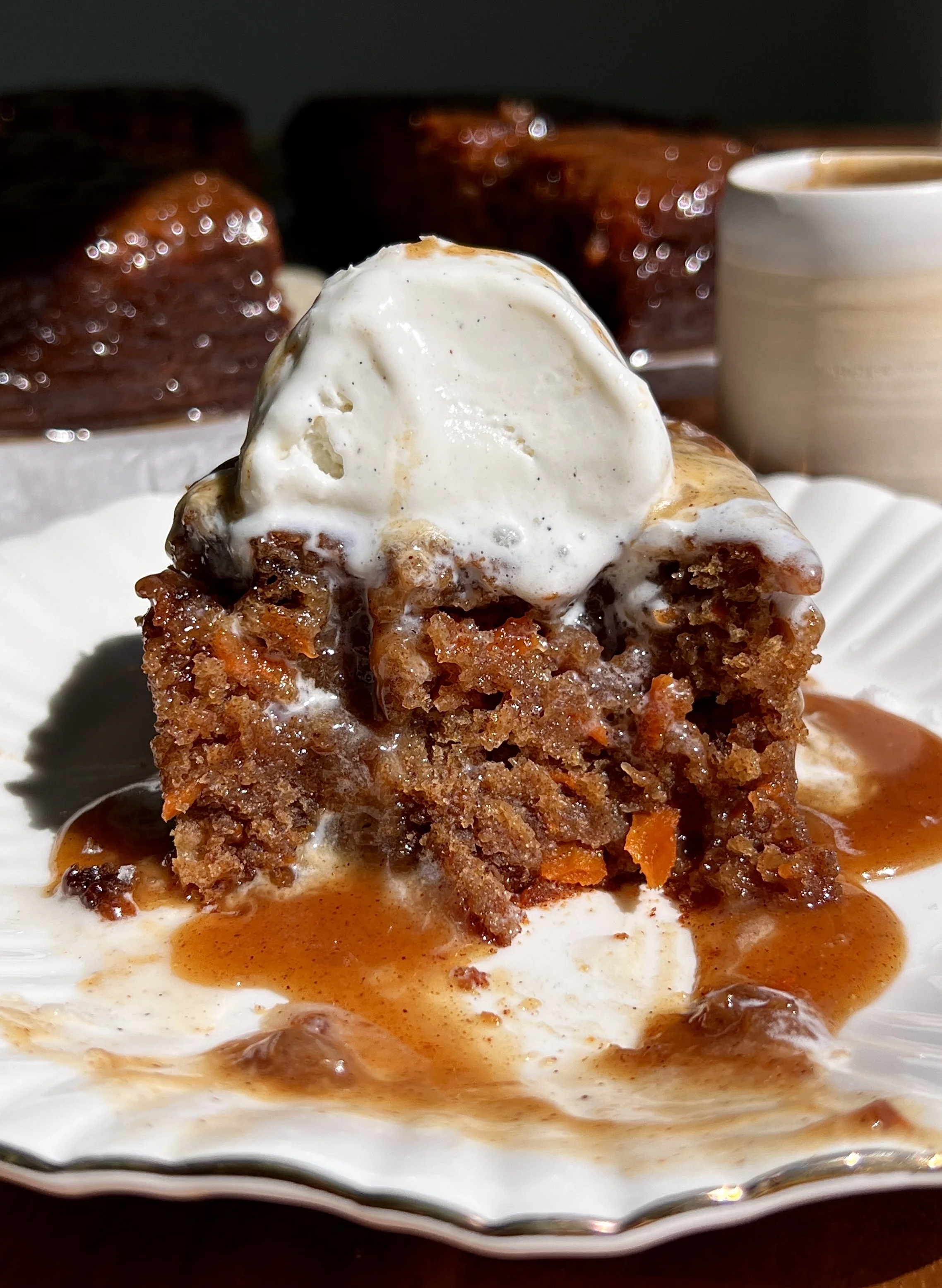Slice of carrot cake sticky toffee pudding with gooey toffee sauce and vanilla ice cream.