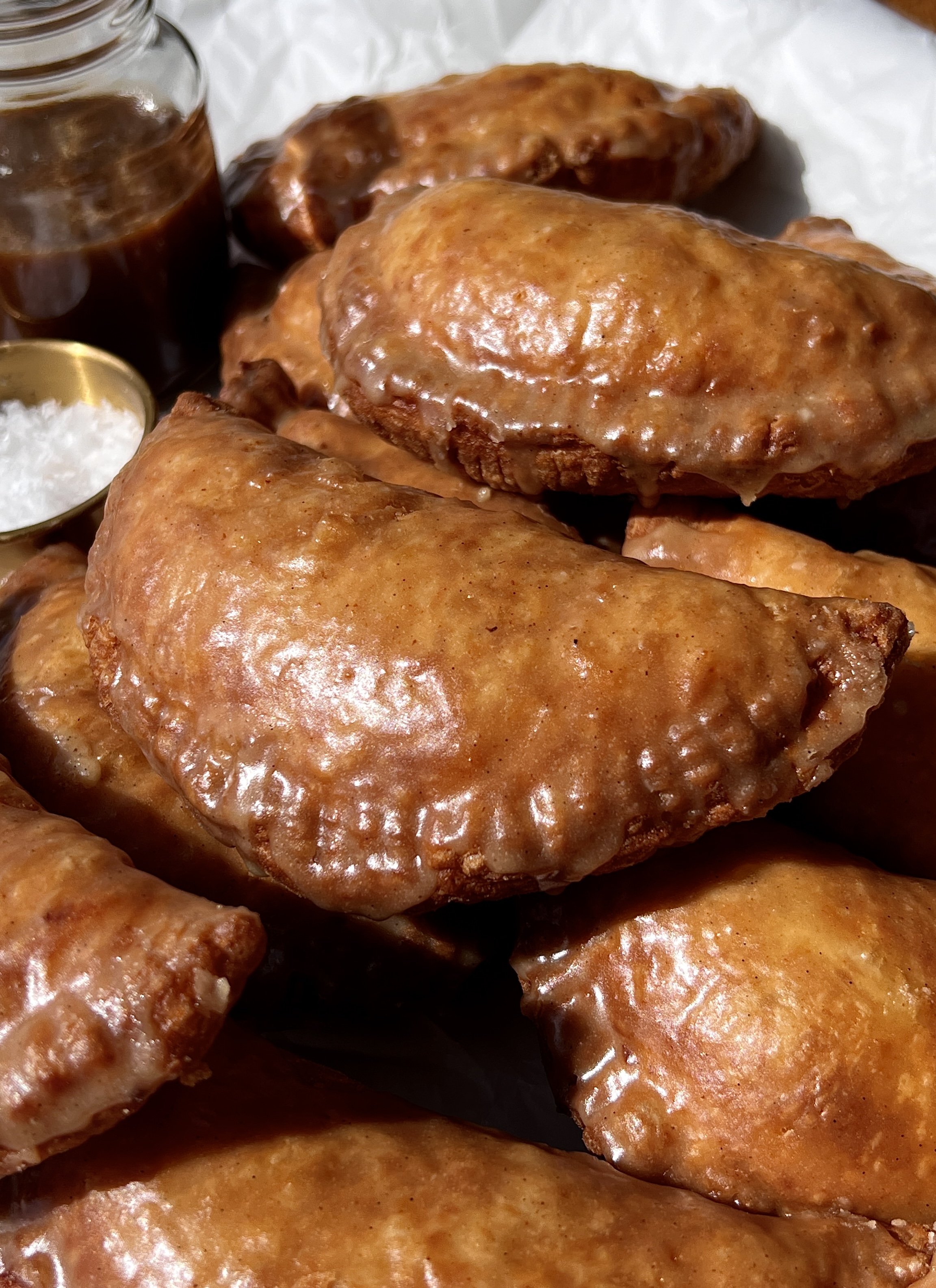 Close-up of a golden fried apple hand pie with a flaky buttery crust and warm and gooey spiced apple pie filling throughout finished with a brown butter maple vanilla bean glaze.