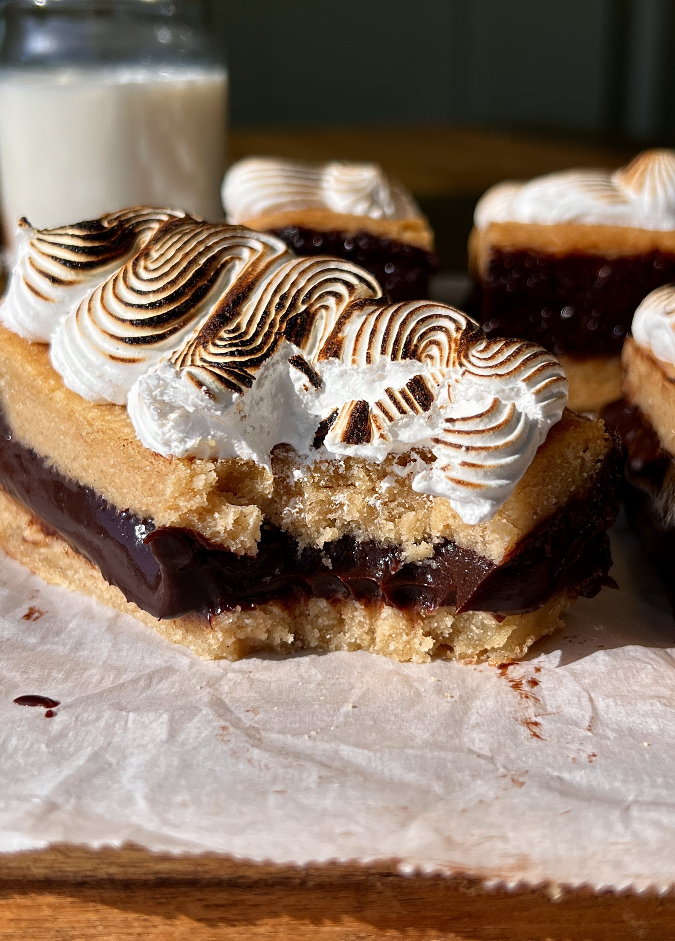 S'mores fudge shortbread bar with a bite taken out showing the soft buttery graham cracker shortbread base, rich fudge layer, and toasted marshmallow creme inside.