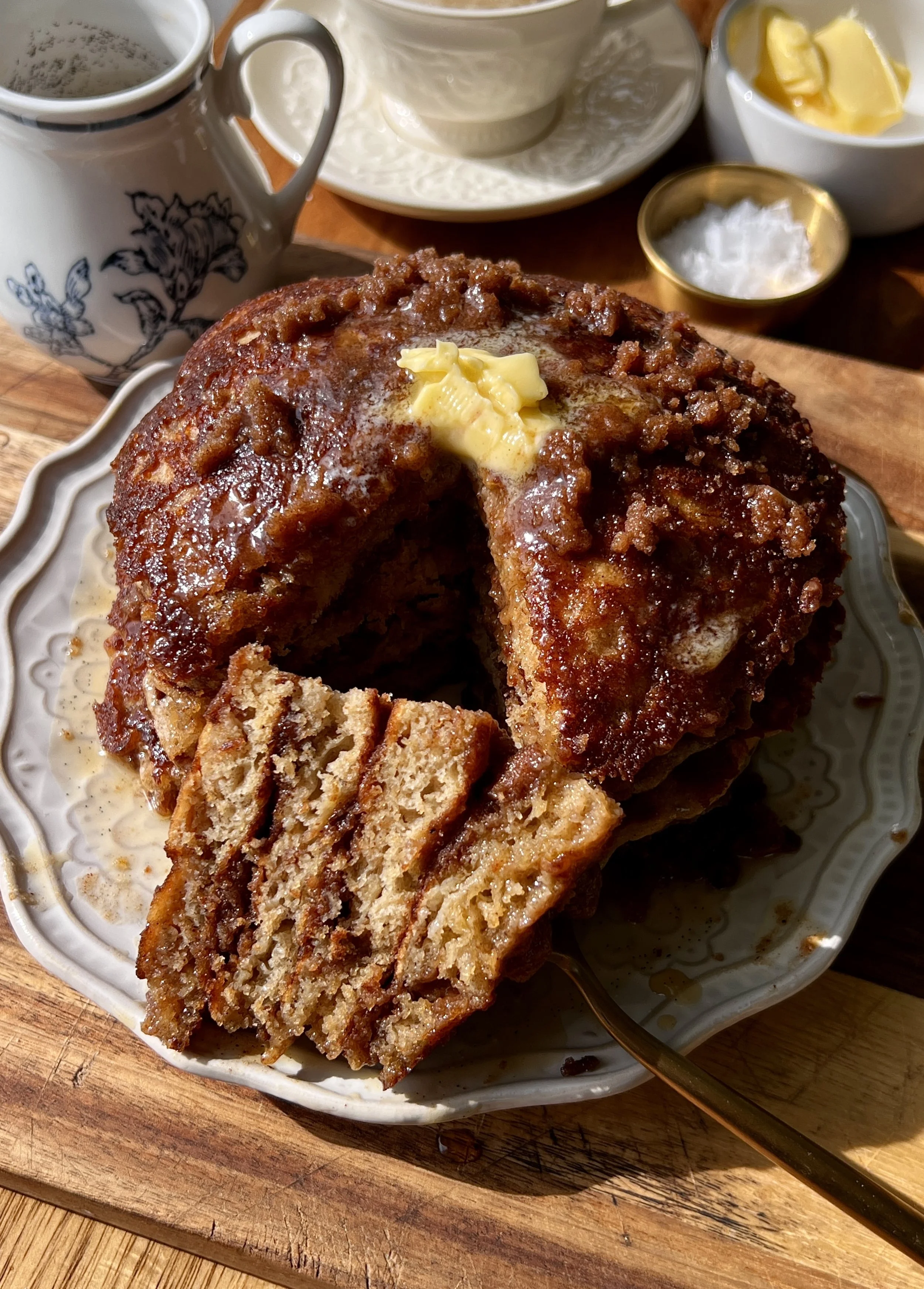 Soft and fluffy banana coffee cake pancakes with a perfectly golden exterior and caramelized cinnamon streusel throughout served warm with a pat of butter, a drizzle of warm vanilla bourbon maple syrup, and a hot cup of coffee.