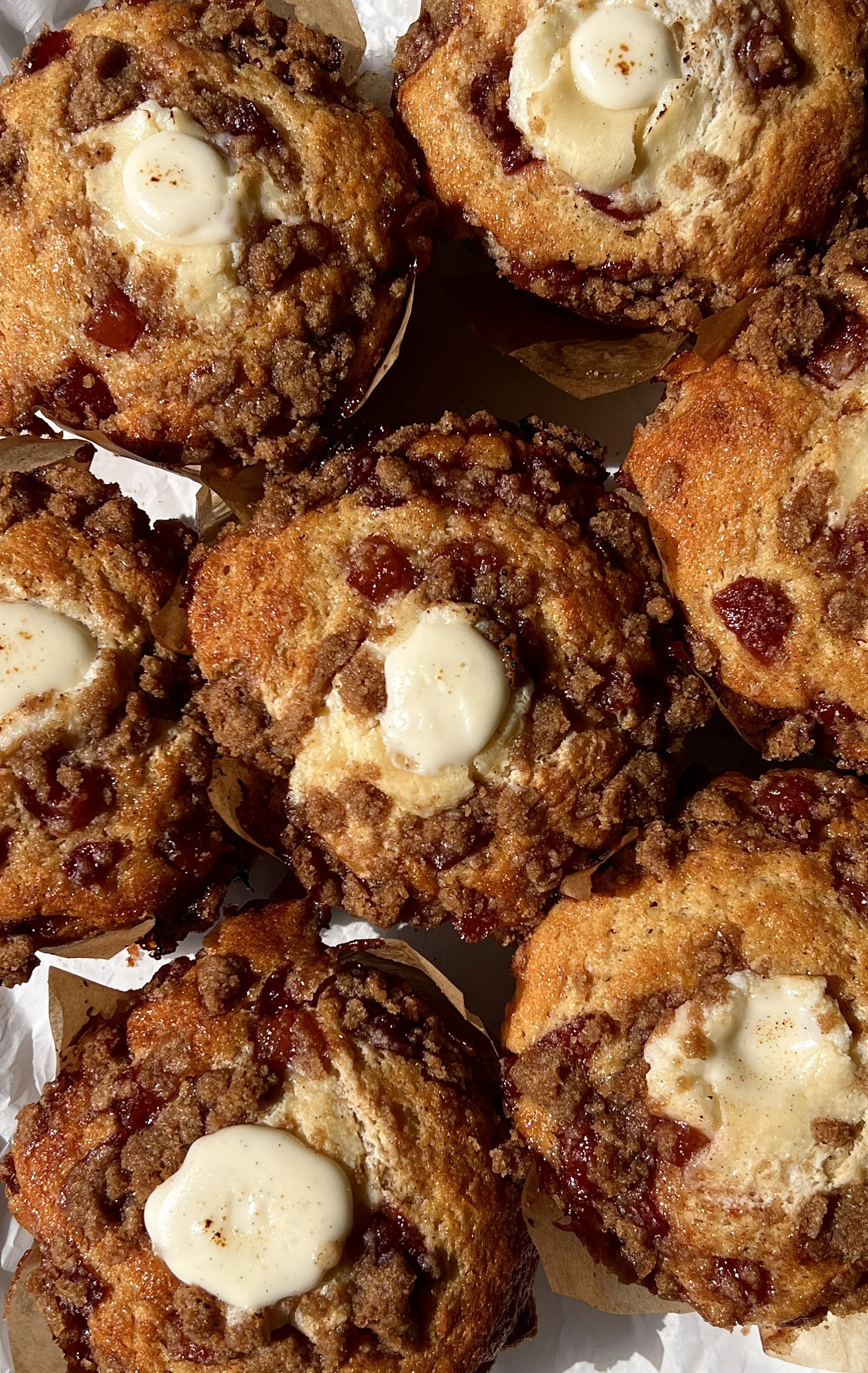 Close-up of a soft and fluffy bakery-style peach cobbler cream cheese muffin with a tender crumb, bright peach flavor, and buttery crumb topping throughout.