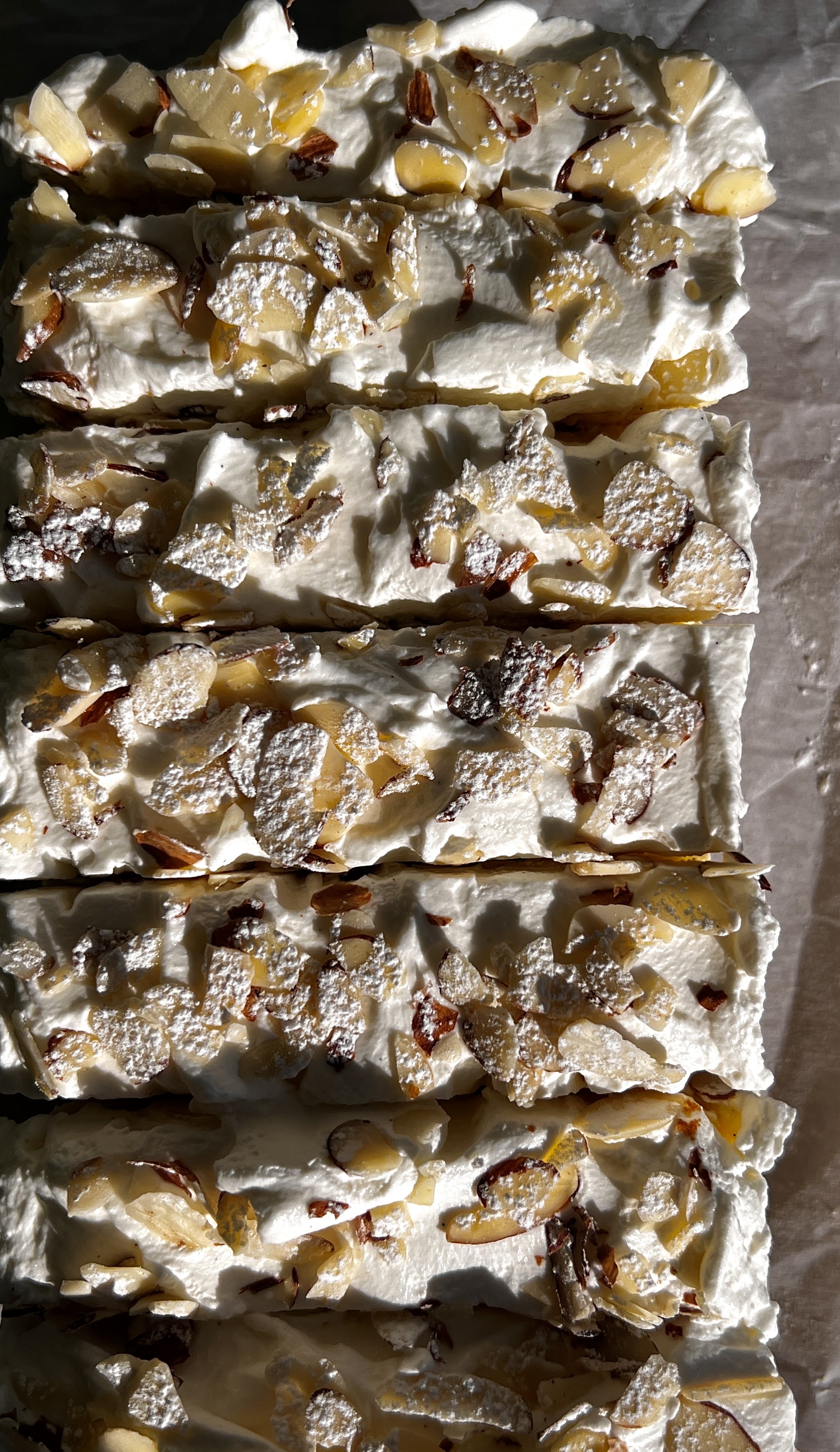 Almond frangipane cheesecake bars with a Biscoff cookie crust, whipped cream, sliced almonds, and powdered sugar.