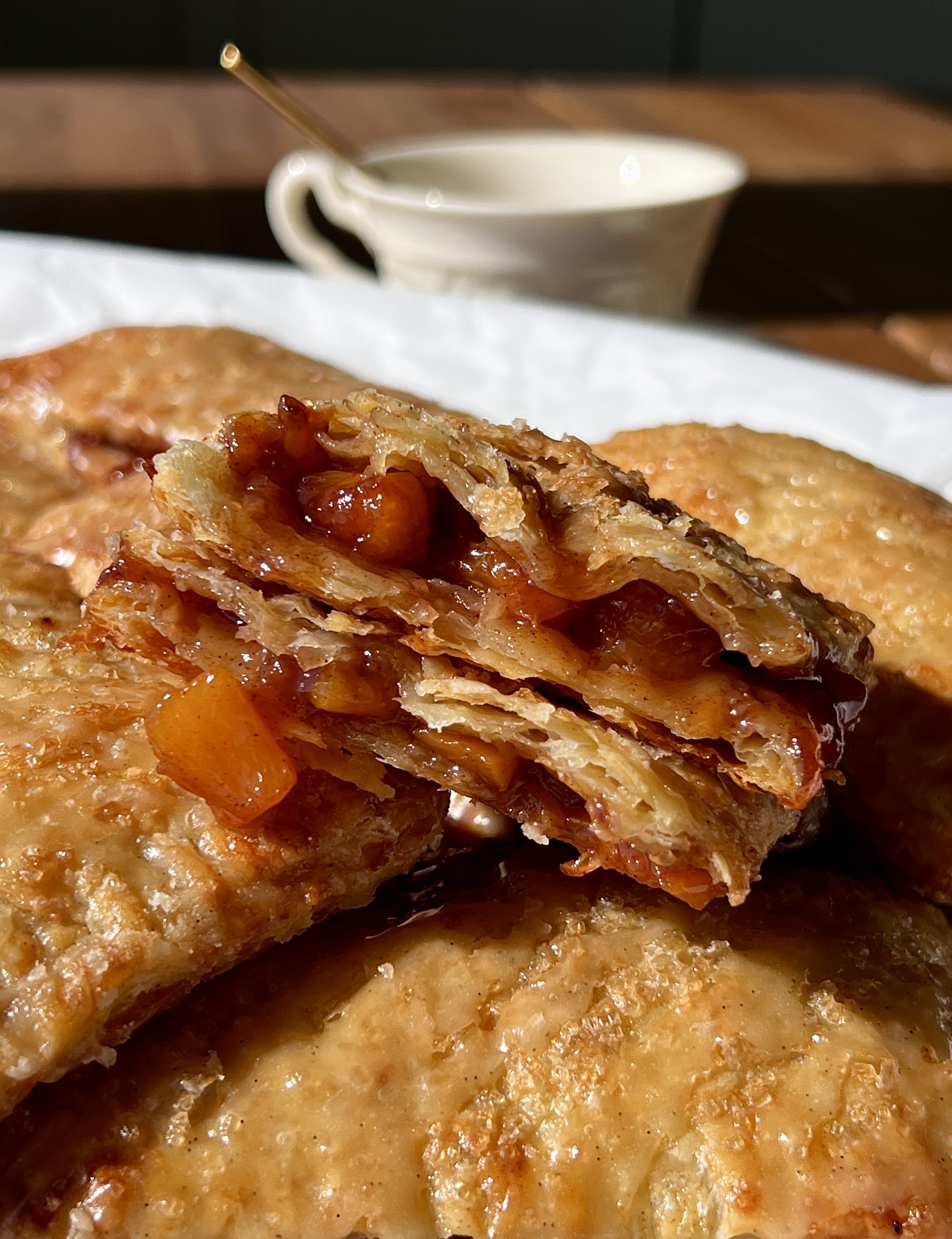 Close-up of a golden and flaky brown sugar peach toaster strudel with homemade puff pastry showing the delicate buttery layers and warm and gooey brown sugar peach filling inside finished with a maple vanilla bean glaze.