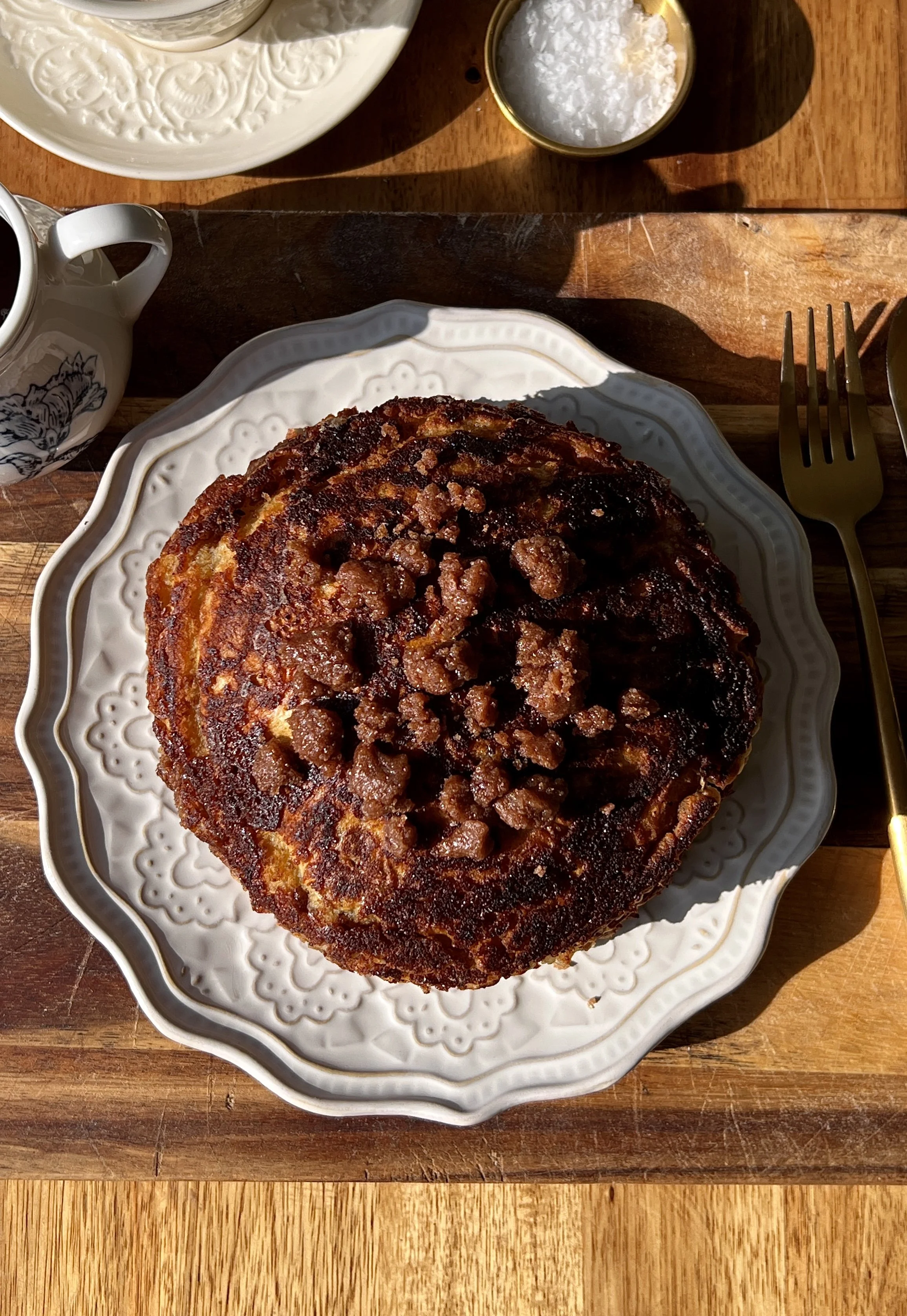 Stack of golden apple streusel griddle cakes with crisp edges, warm gooey apple filling, and caramelized cinnamon streusel served warm with a pat of butter, a drizzle of maple syrup, and a hot cup of coffee.