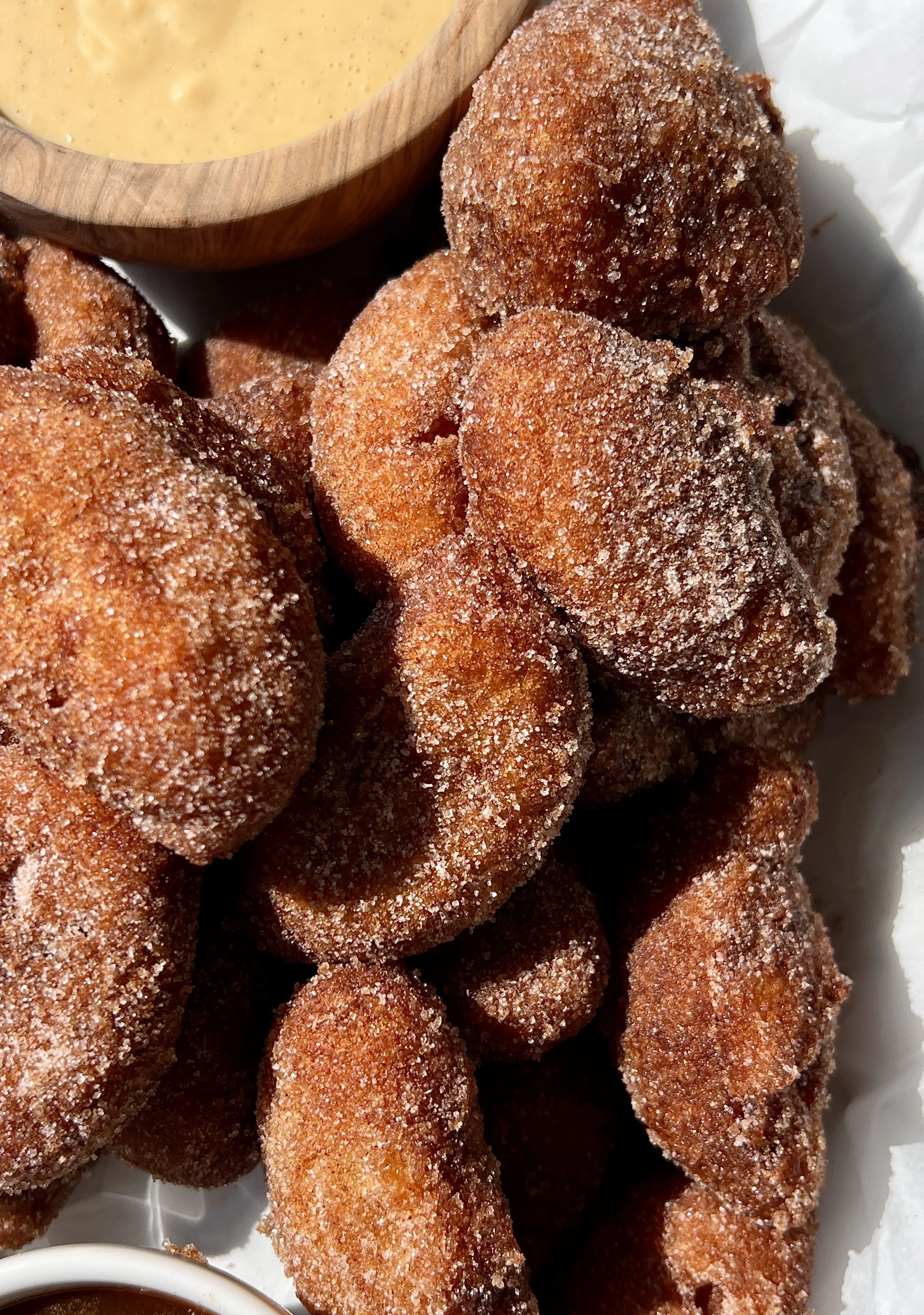 Close-up of a golden and crisp buttermilk fried peach rolled in cinnamon sugar with a warm and juicy peach inside served with crème anglaise and salted caramel.