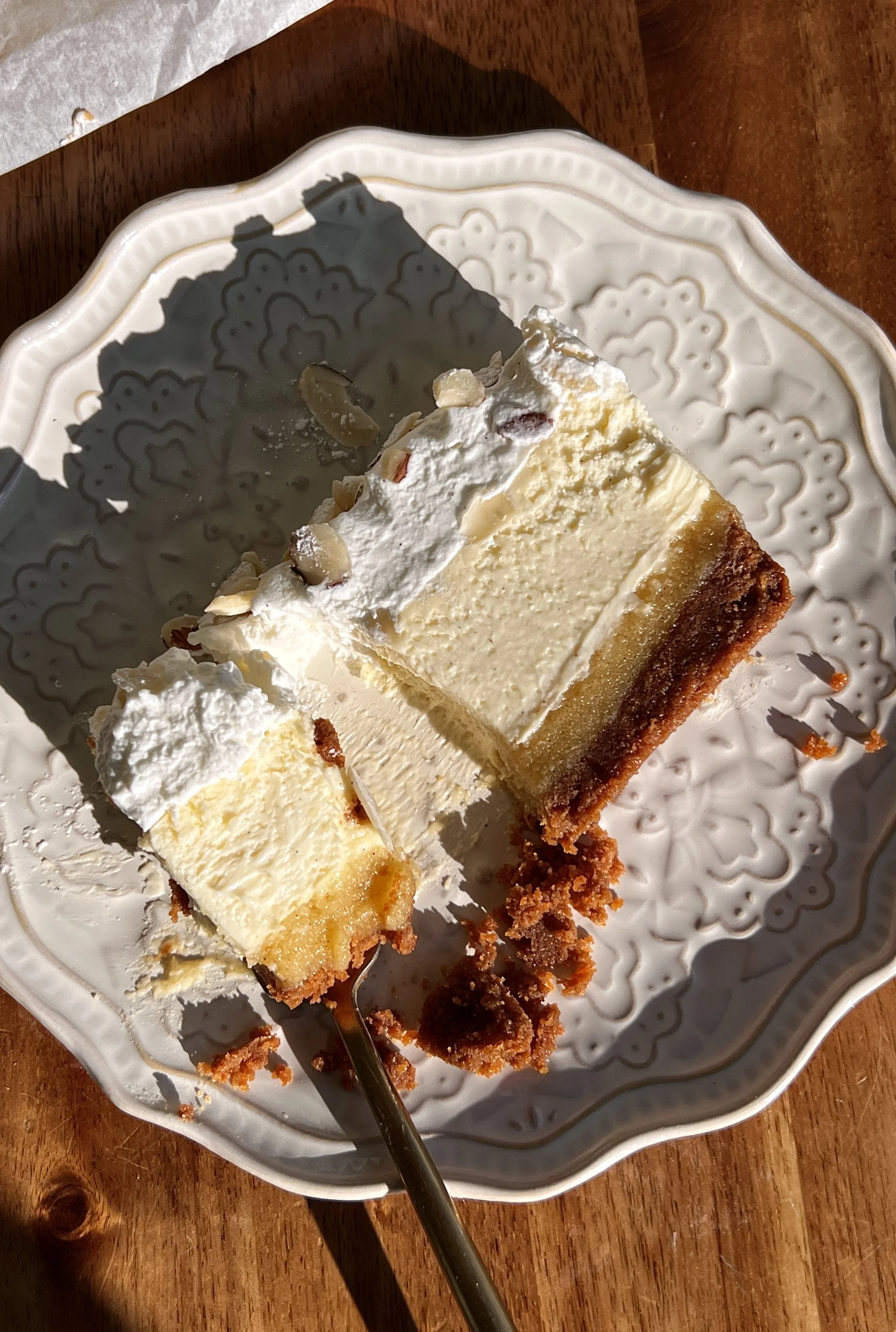 Almond frangipane cheesecake bars topped with whipped cream, sliced almonds, and powdered sugar.