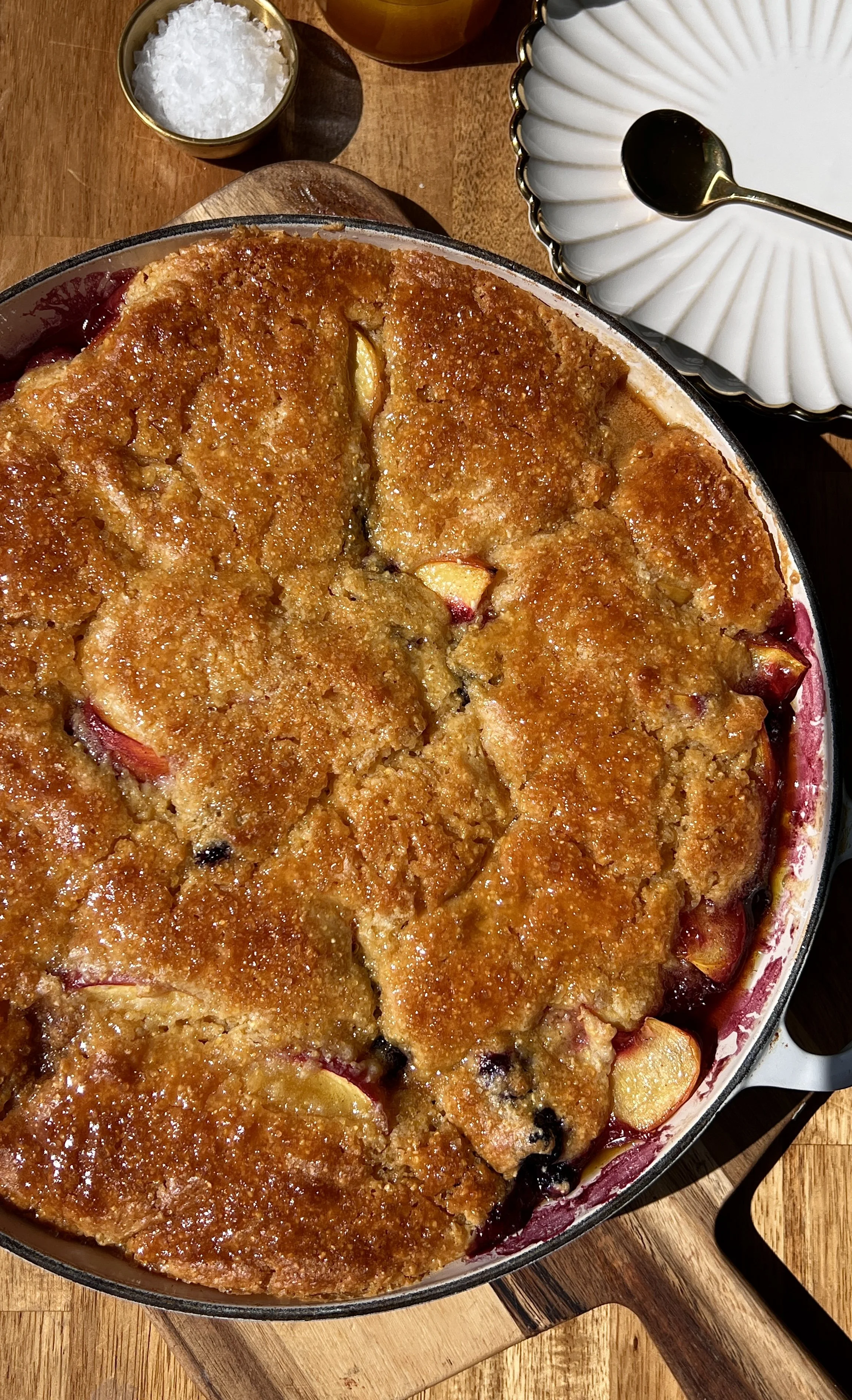 Close-up of a golden and crisp blueberry peach cornbread cobbler showing the buttery cornbread topping with warm and juicy peaches and bright tart blueberries bubbling up throughout.
