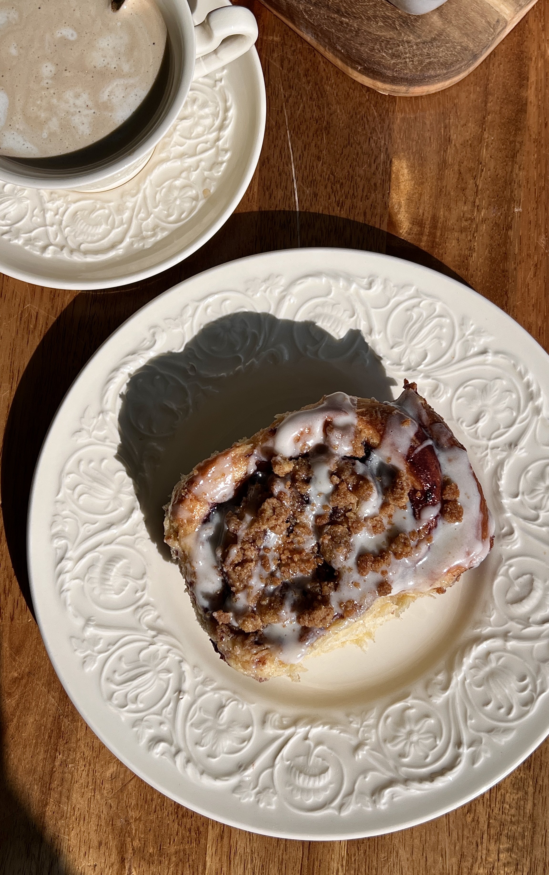 Warm blueberry crumble cinnamon rolls served with cream cheese glaze and a cup of coffee.