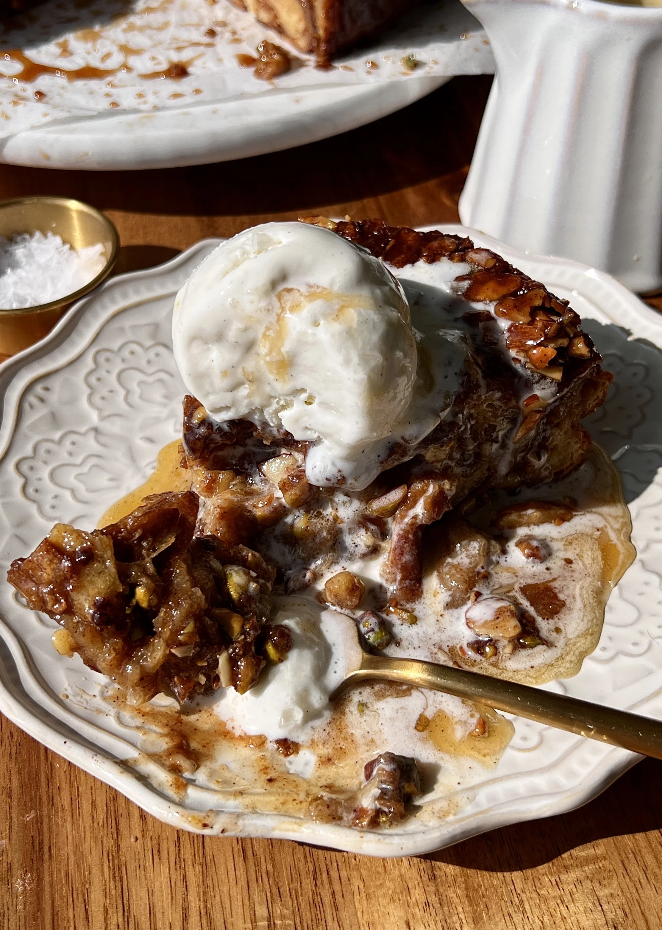 Golden baklava croissant bread pudding made with buttery flaky croissants and vanilla bean custard swirled with a warm gooey baklava filling served warm with a scoop of vanilla ice cream, honey buttermilk syrup, and flaky sea salt.