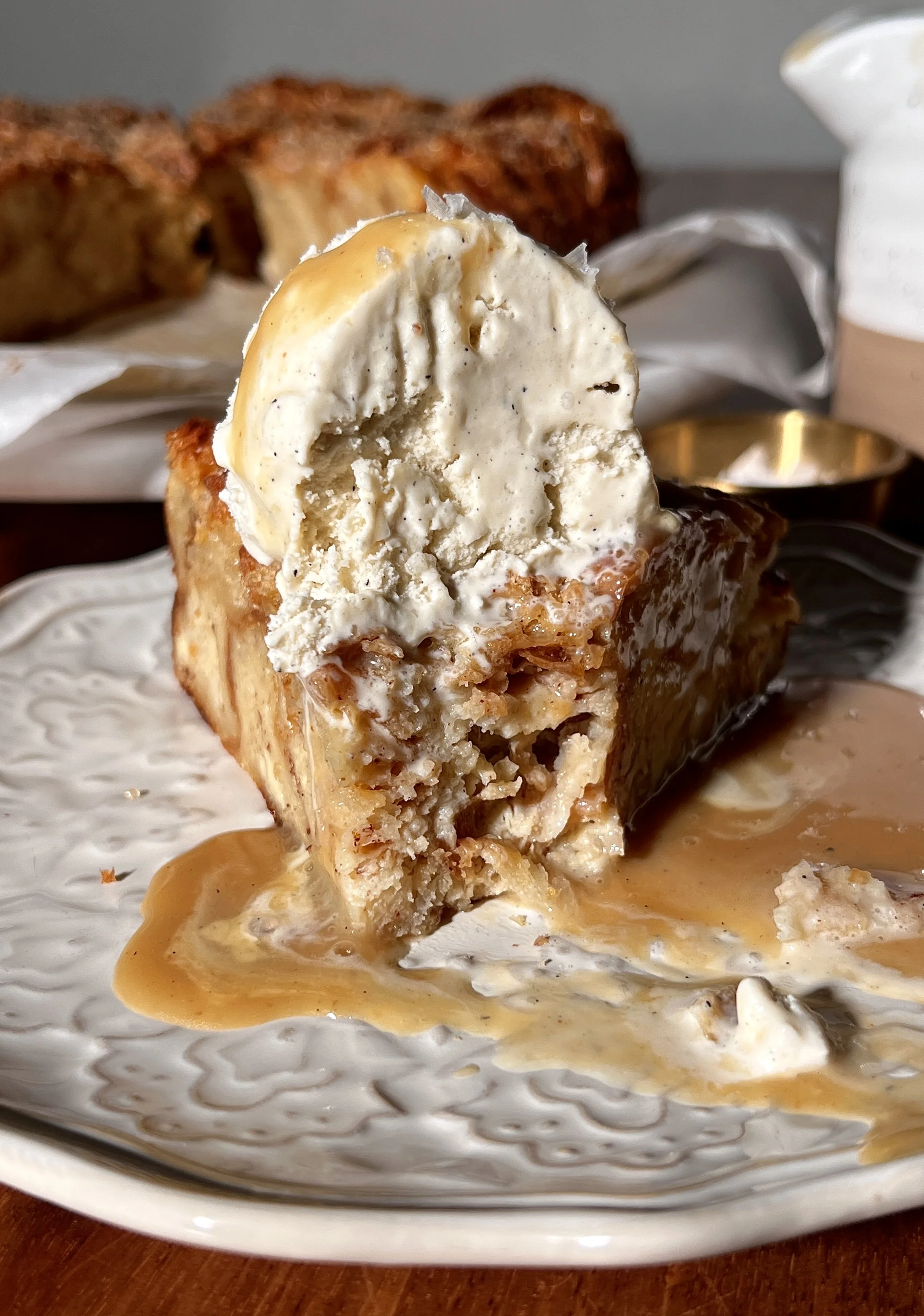Warm vanilla bean croissant bread pudding with a golden crisp top, served with buttered caramel rum sauce and a scoop of vanilla ice cream.