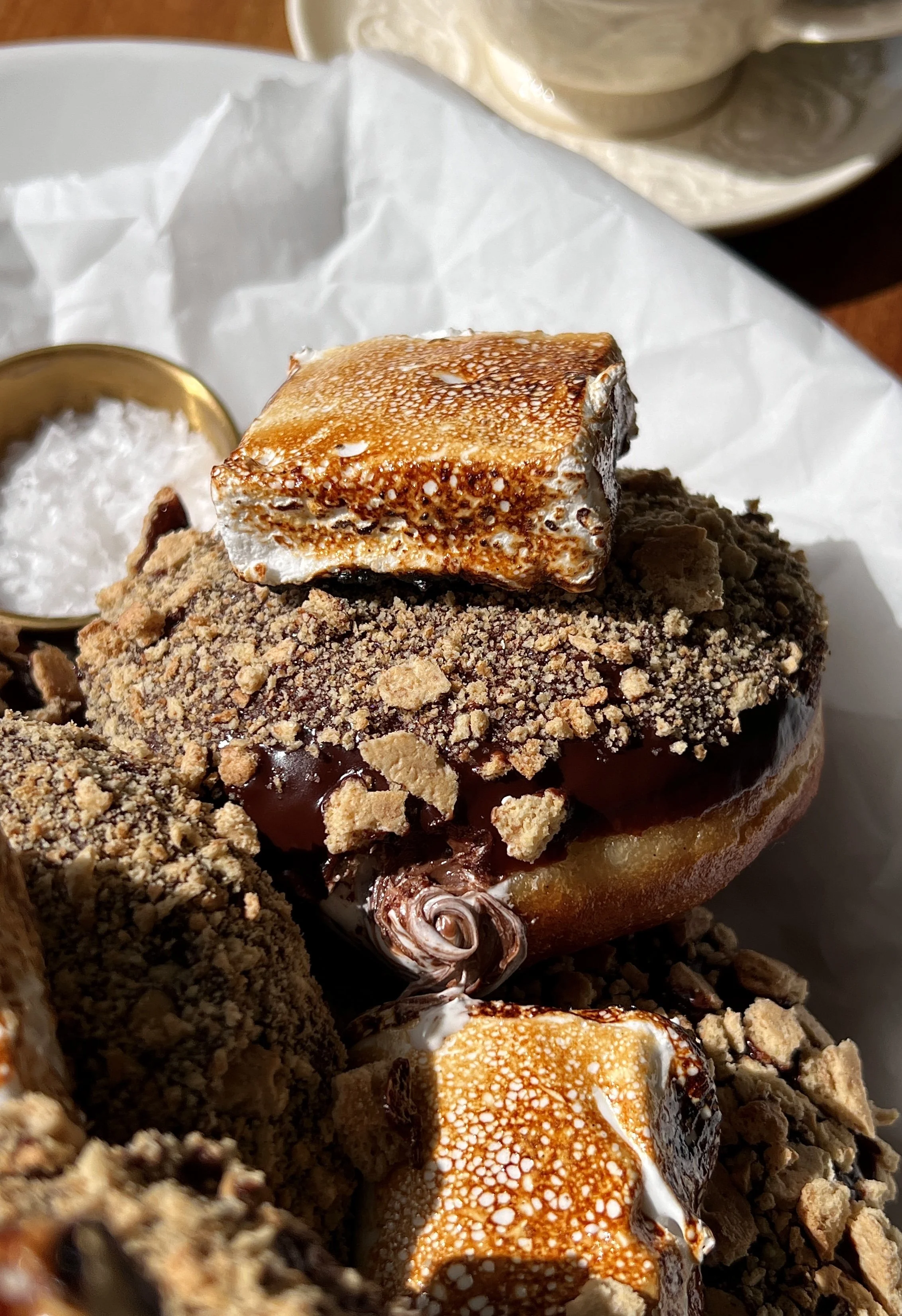 Close-up of a pillowy soft and fluffy s'mores donut with a golden exterior filled with marshmallow buttercream and Nutella finished with chocolate ganache and a toasted marshmallow.