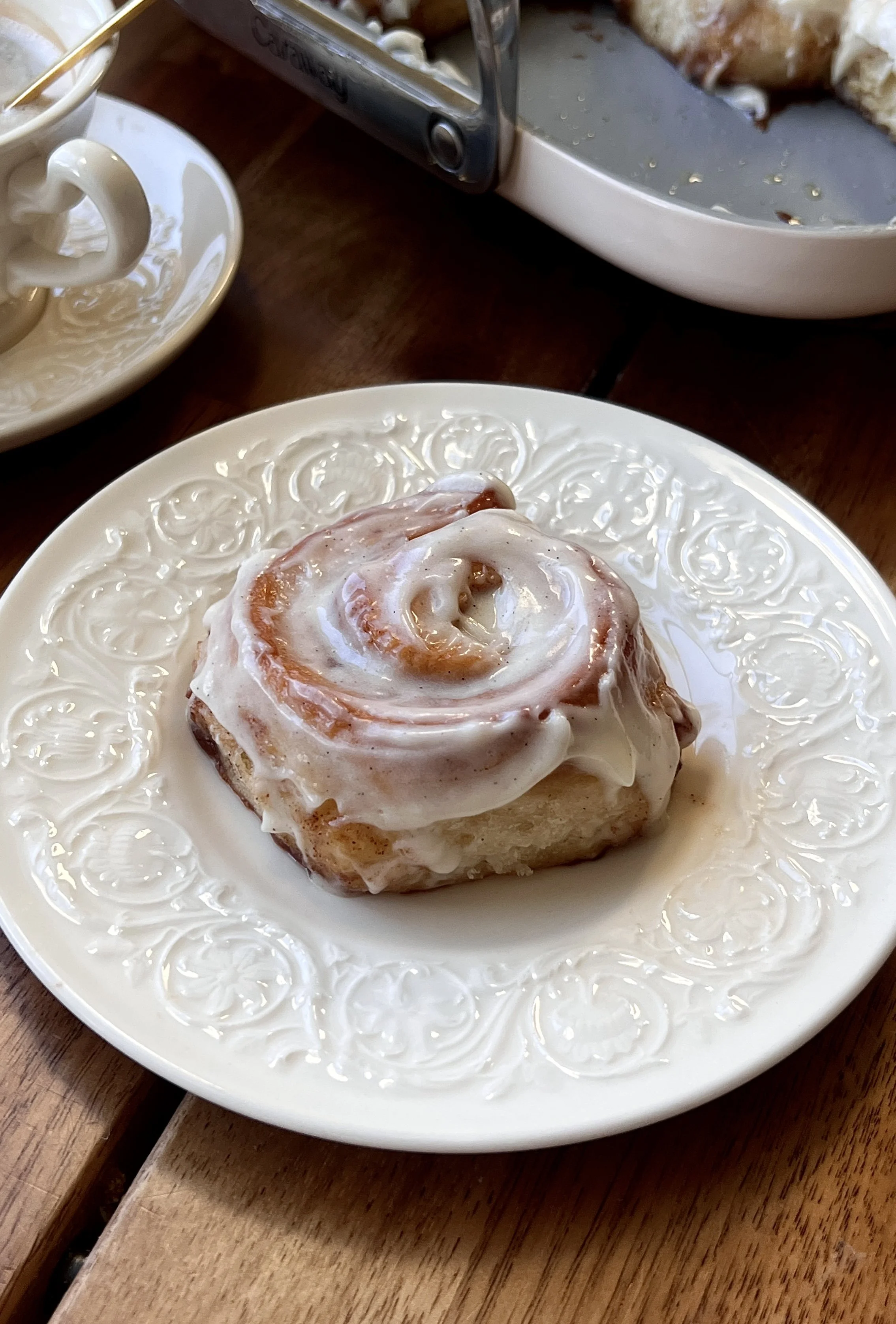 Close-up of Mini Classic Cinnamon Rolls topped with cream cheese frosting and served warm with coffee