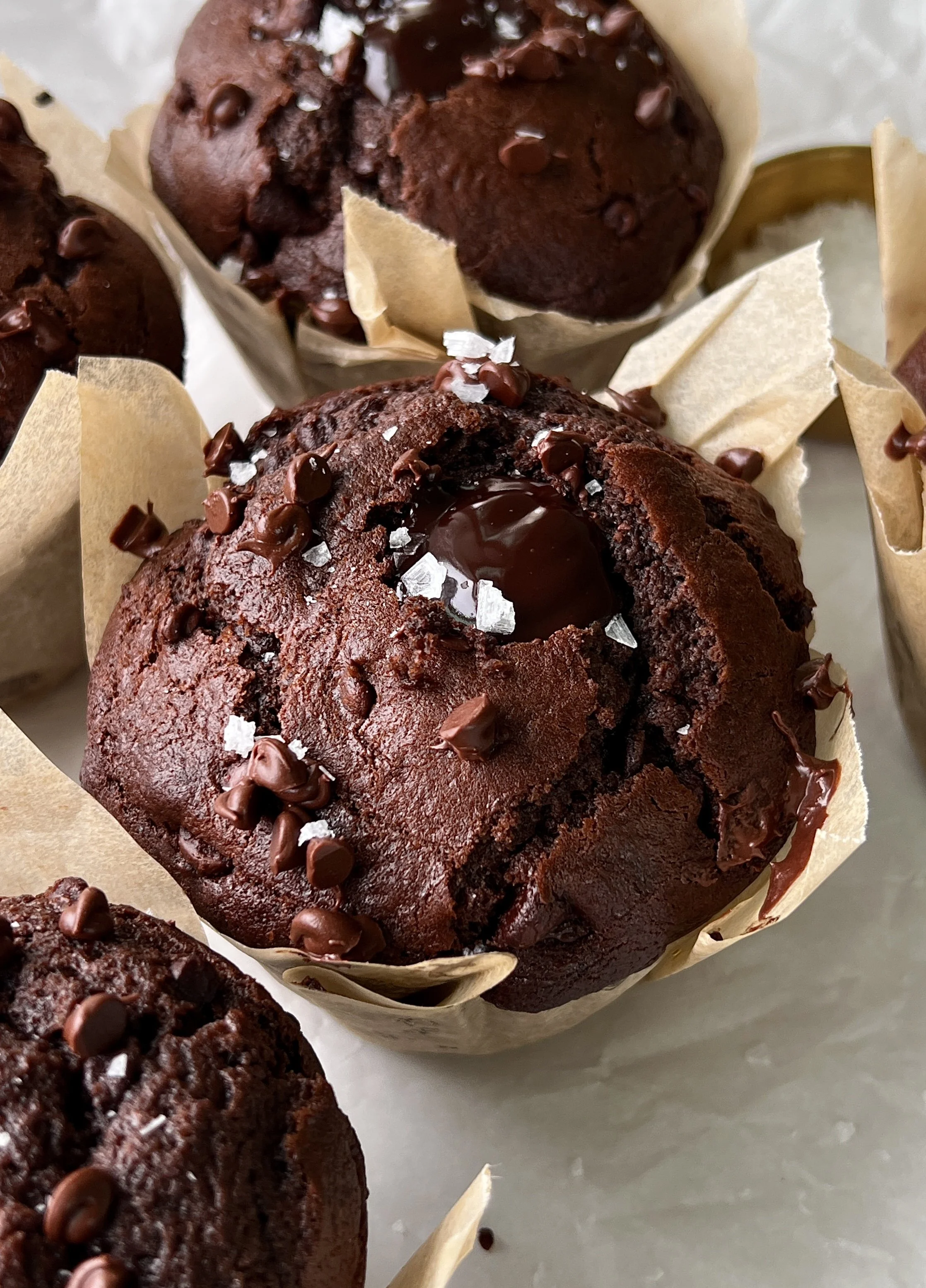 Close-up of a bakery-style triple chocolate fudge muffin with a soft and fluffy crumb, melty chocolate chips throughout, and a molten chocolate ganache center.