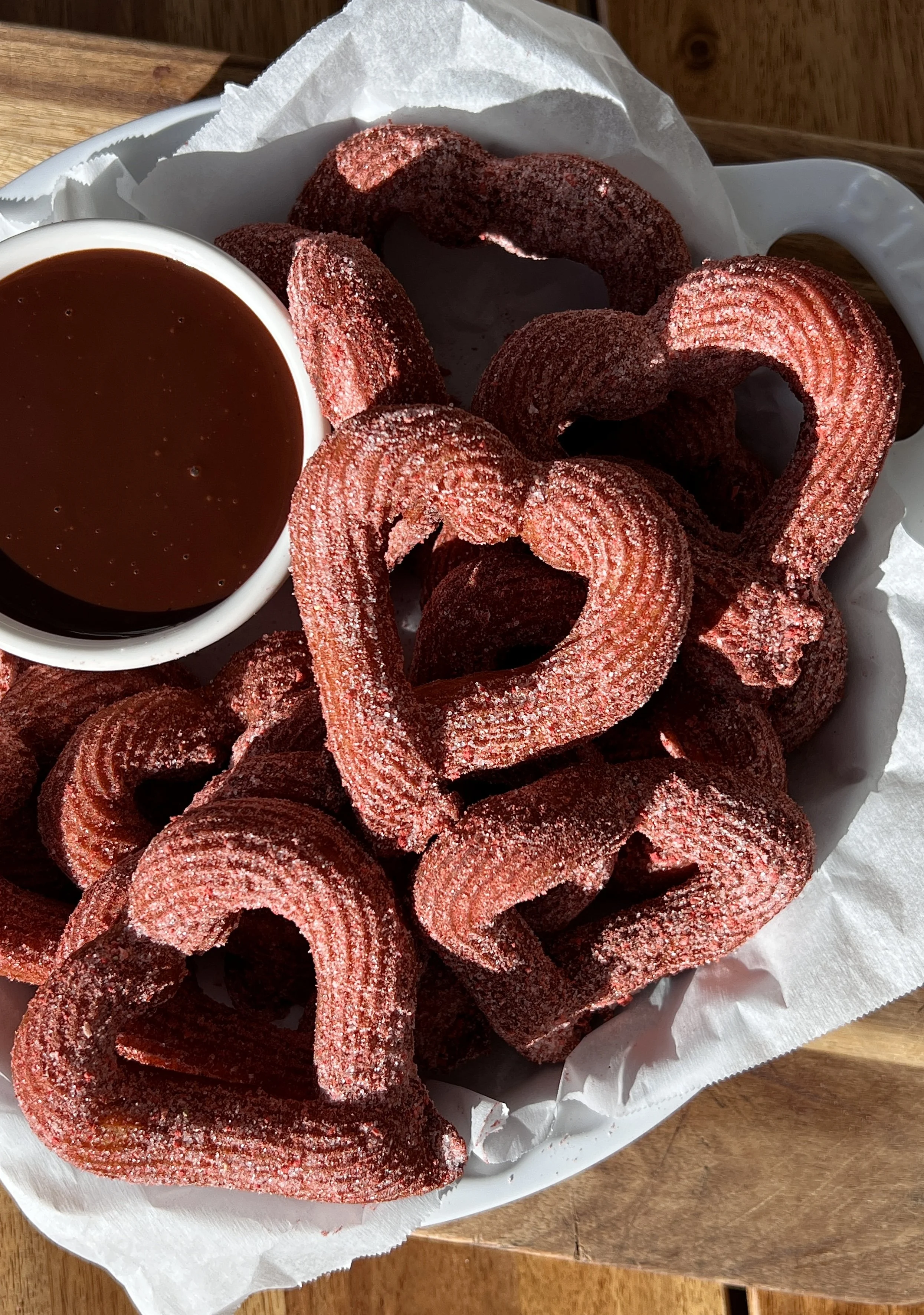 Heart-shaped churros coated in pink strawberry cinnamon sugar and served warm with homemade chocolate sauce.