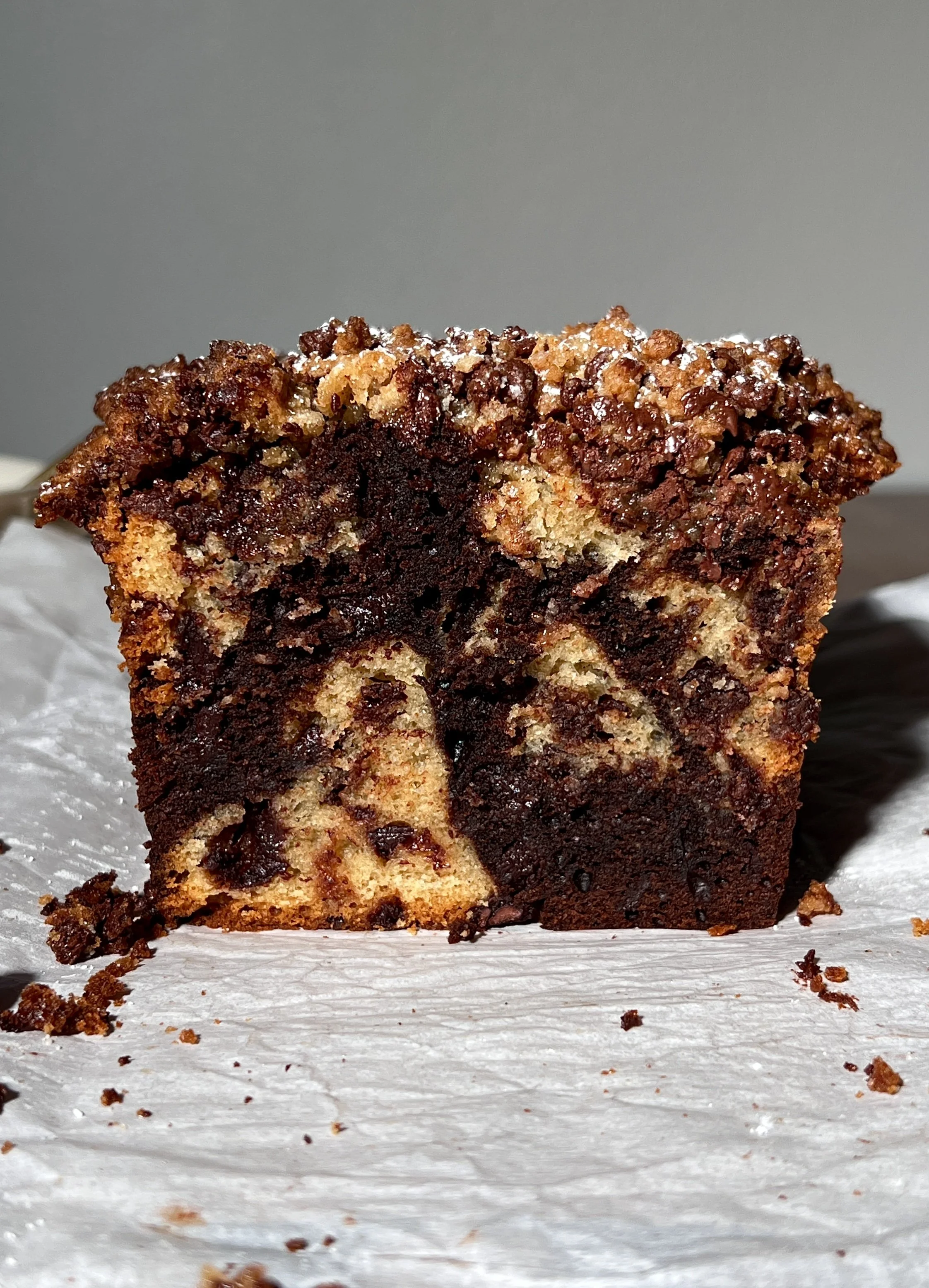 Brown butter marbled chocolate chip crumb loaf cake sliced and served warm, showing vanilla and chocolate swirled crumb, melty chocolate chips, and a buttery crumb topping, finished with flaky sea salt and coffee on the side.