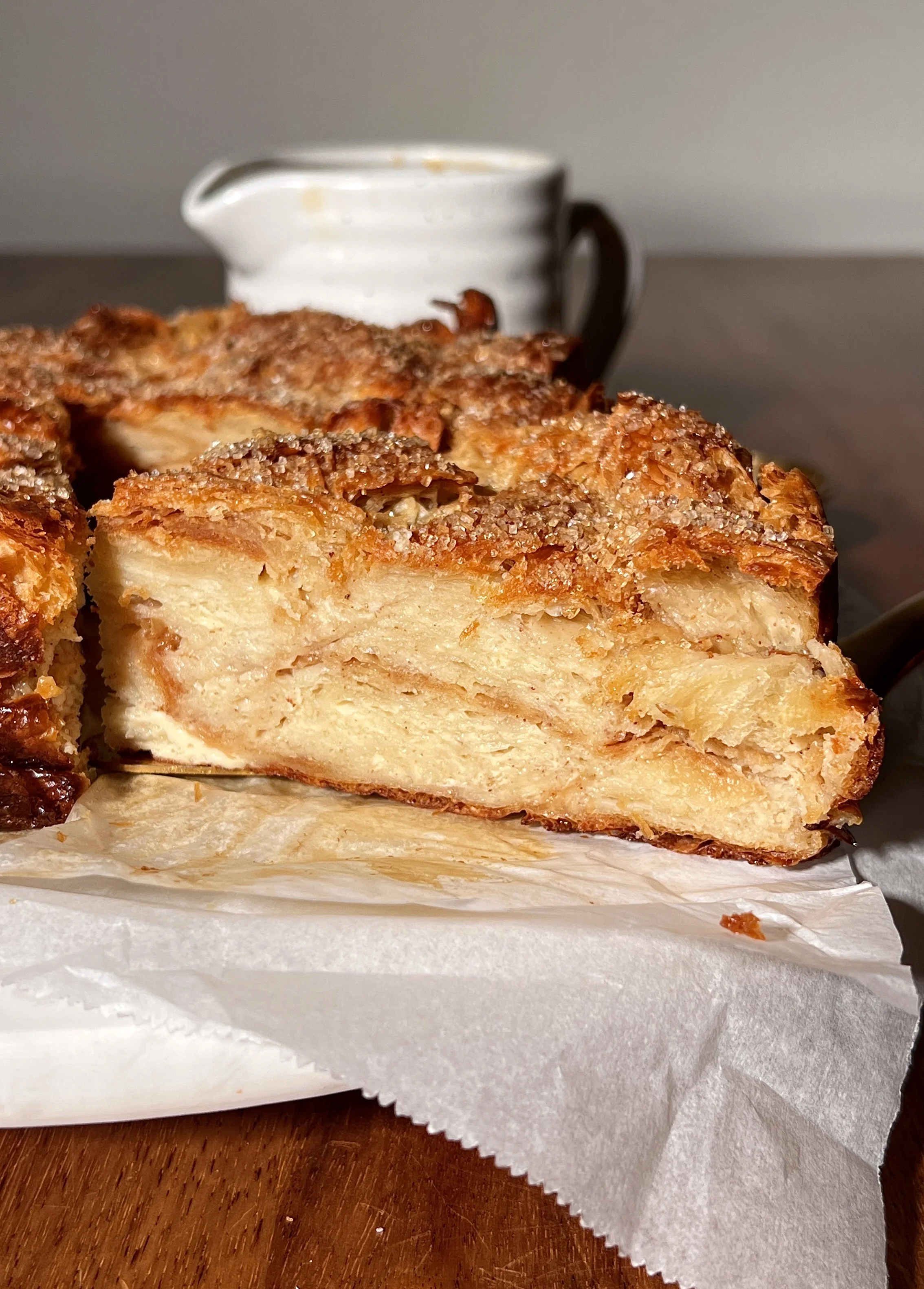 Warm vanilla bean croissant bread pudding with a golden crisp top, served with buttered caramel rum sauce and a scoop of vanilla ice cream.