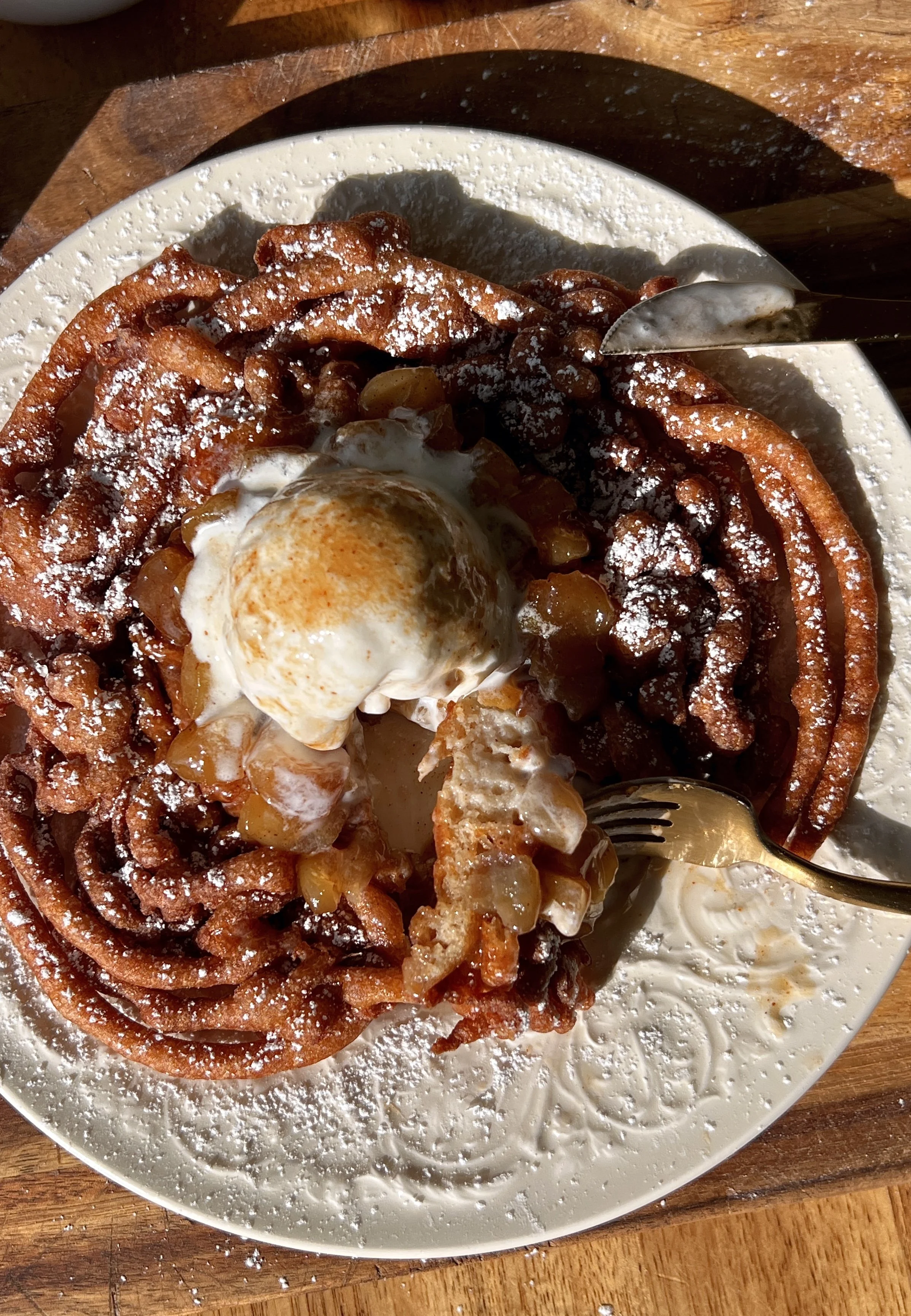 Soft and tender apple cider funnel cakes with a perfectly golden and crisp exterior served warm with a dusting of powdered sugar a gooey apple topping a scoop of vanilla ice cream and a drizzle of salted caramel.