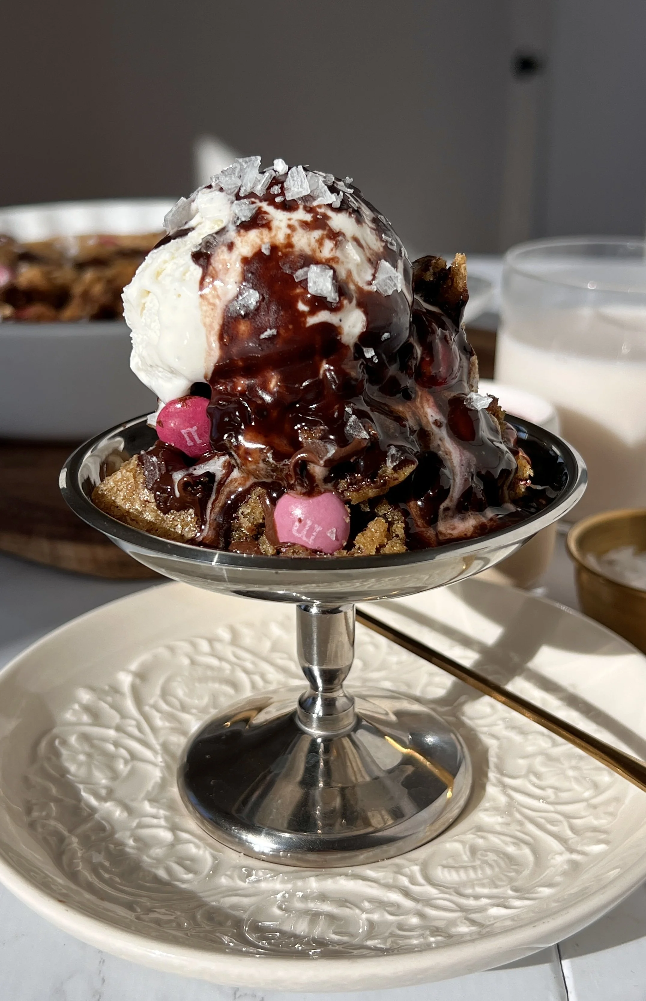 Scoopable brown butter chocolate chip cookies baked in a pan with gooey centers, vanilla ice cream, and hot fudge sauce.