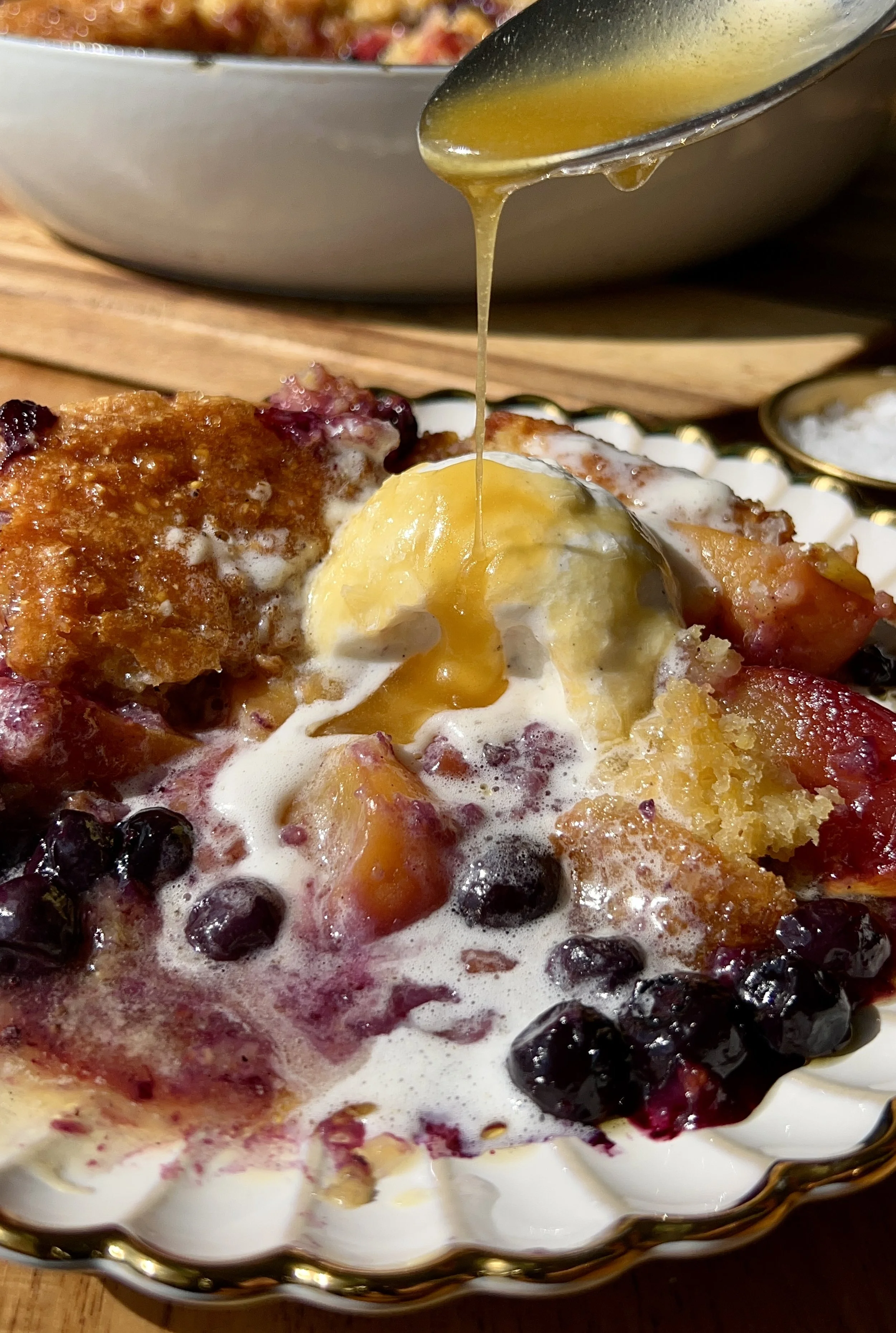 Warm and golden blueberry peach cornbread cobbler brushed with melted honey butter served with a scoop of vanilla ice cream, an extra drizzle of honey butter, and a sprinkle of flaky sea salt as the ultimate summer dessert.