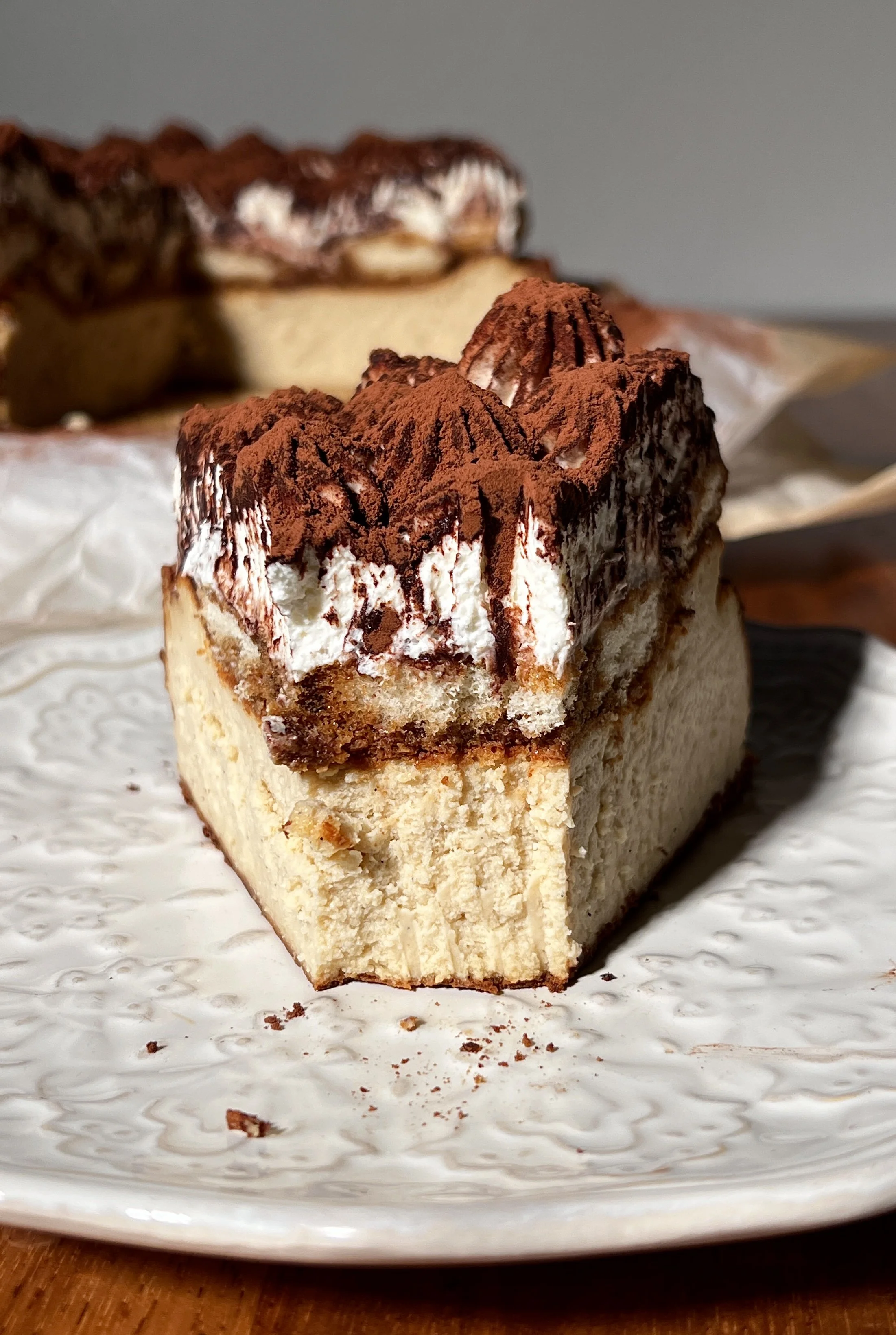 Tiramisu basque cheesecake topped with espresso-soaked ladyfingers, creamy mascarpone layer, and a generous dusting of cocoa powder.