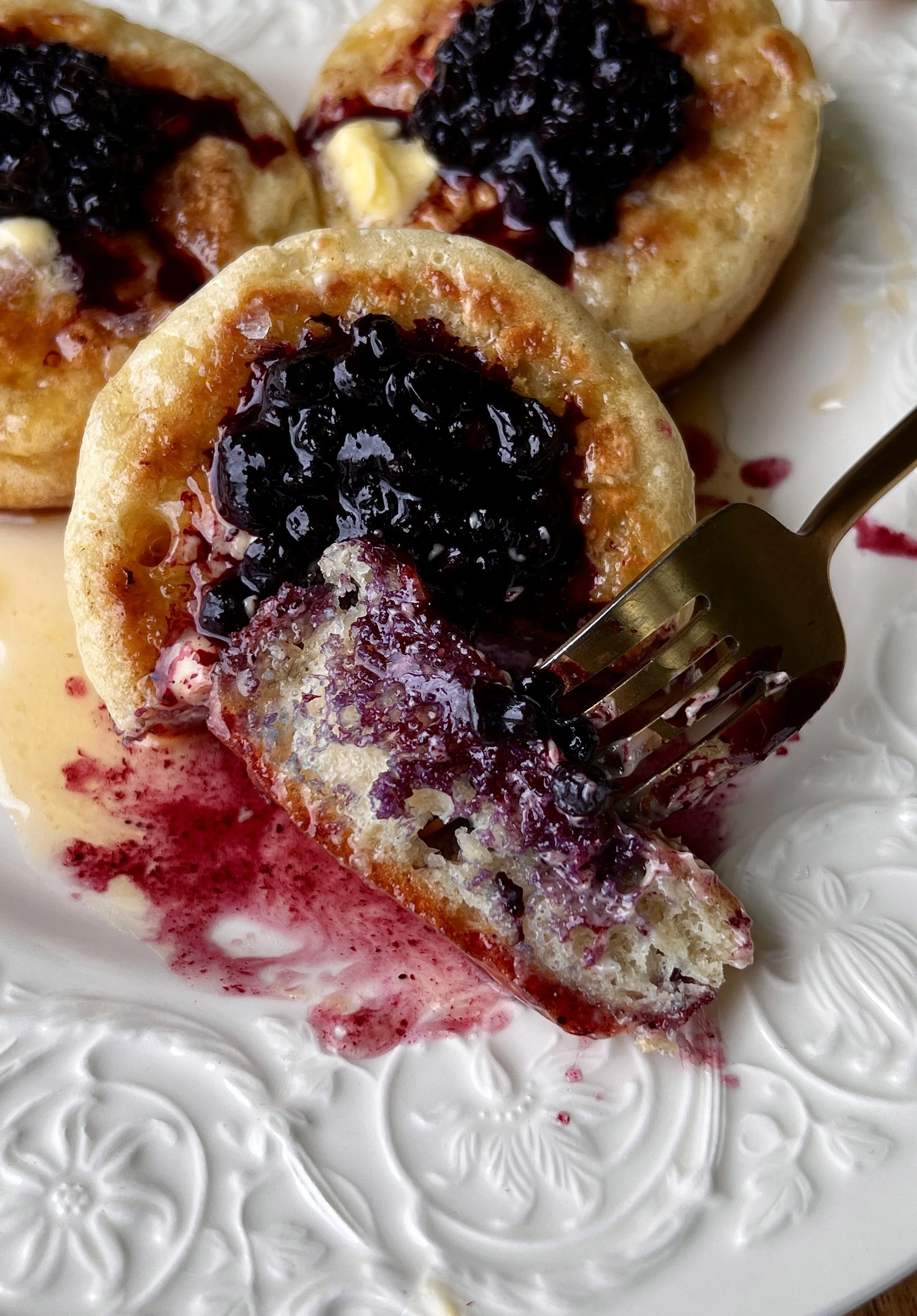Soft and fluffy homemade crumpets cooked to a gorgeous golden and served warm with butter, bright blueberry compote, a drizzle of honey, and a hot cup of coffee.