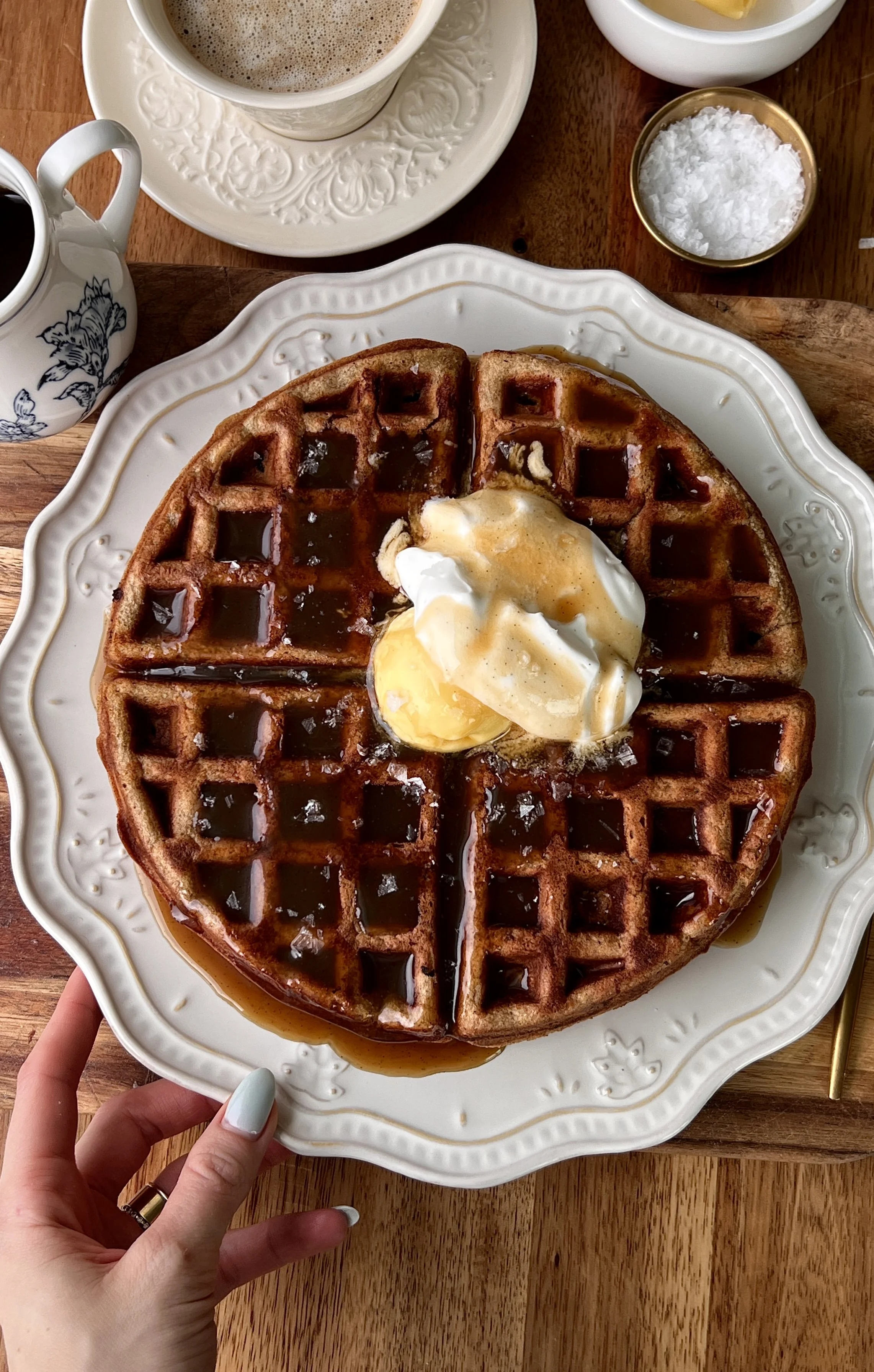 Sticky toffee waffles served warm with butter, whipped sour cream topping, and a drizzle of silky maple toffee sauce with a hot cup of coffee.
