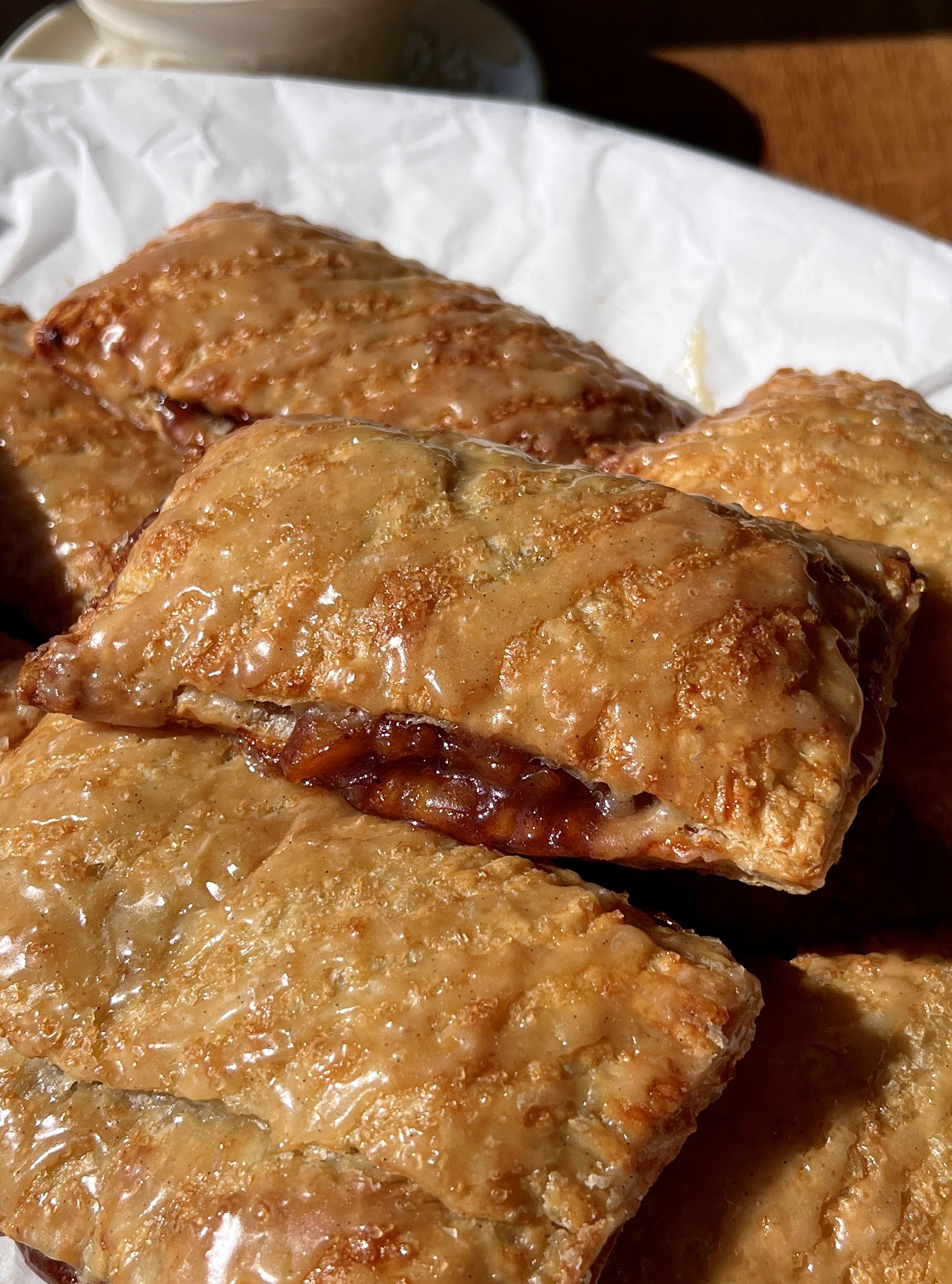 Close-up of a golden and flaky brown sugar peach toaster strudel with homemade puff pastry showing the delicate buttery layers and warm and gooey brown sugar peach filling inside finished with a maple vanilla bean glaze.