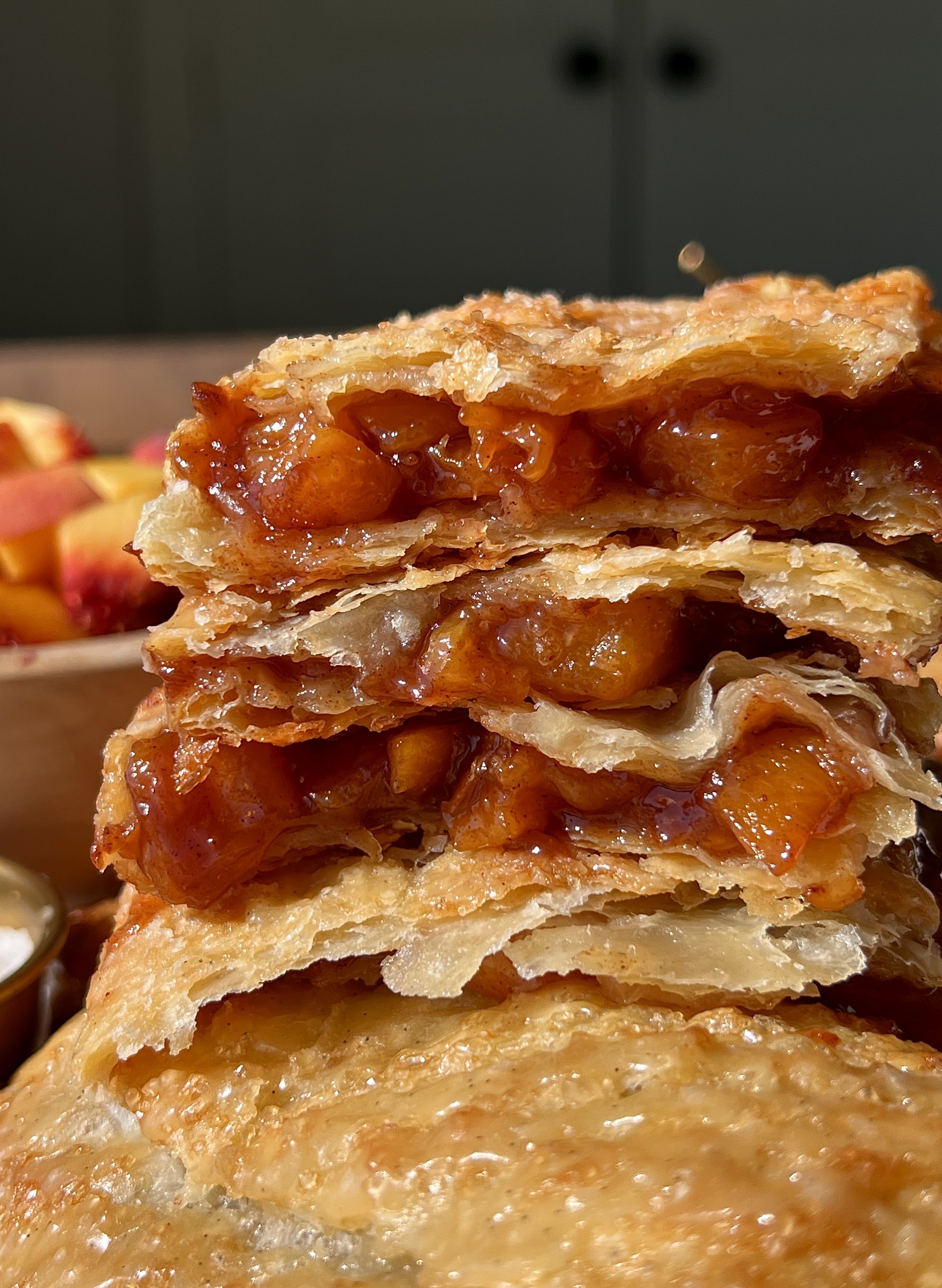 Close-up of a golden and flaky brown sugar peach toaster strudel with homemade puff pastry showing the delicate buttery layers and warm and gooey brown sugar peach filling inside finished with a maple vanilla bean glaze.
