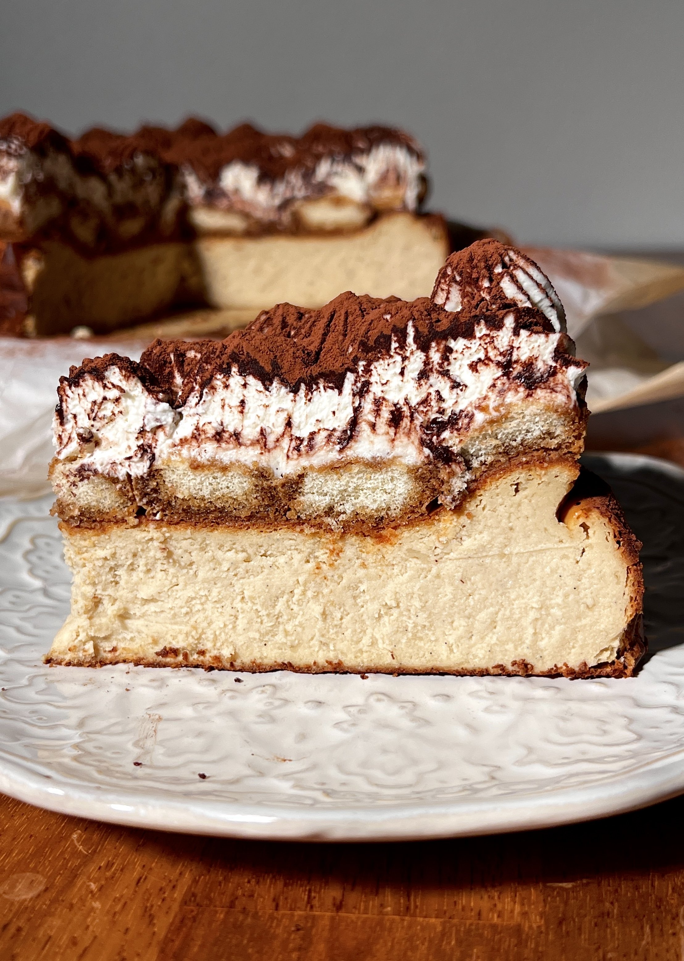 Tiramisu basque cheesecake topped with espresso-soaked ladyfingers, creamy mascarpone layer, and a generous dusting of cocoa powder.