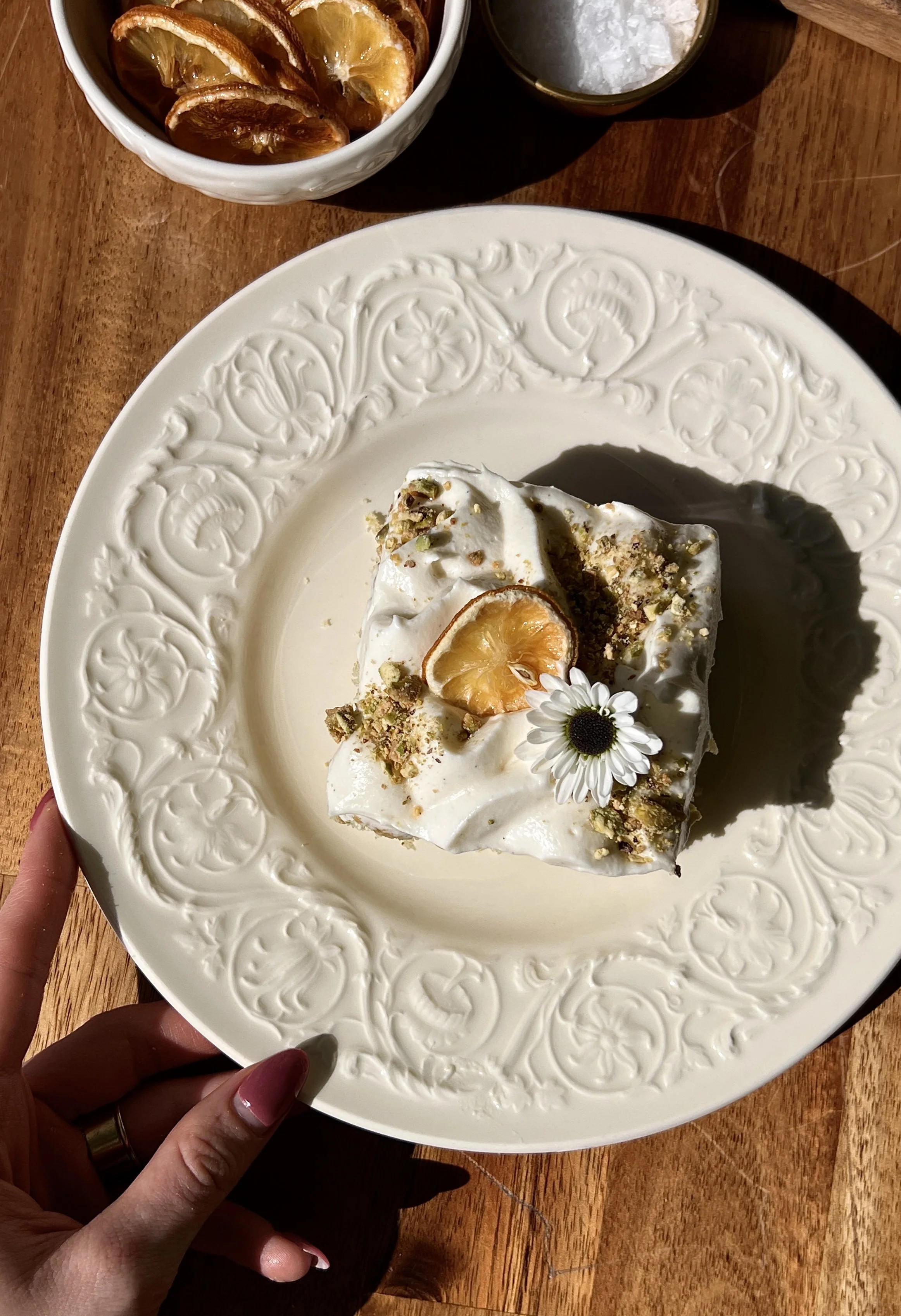Slice of lemon curd pistachio cake with cream cheese frosting and a sprinkle of chopped pistachios.