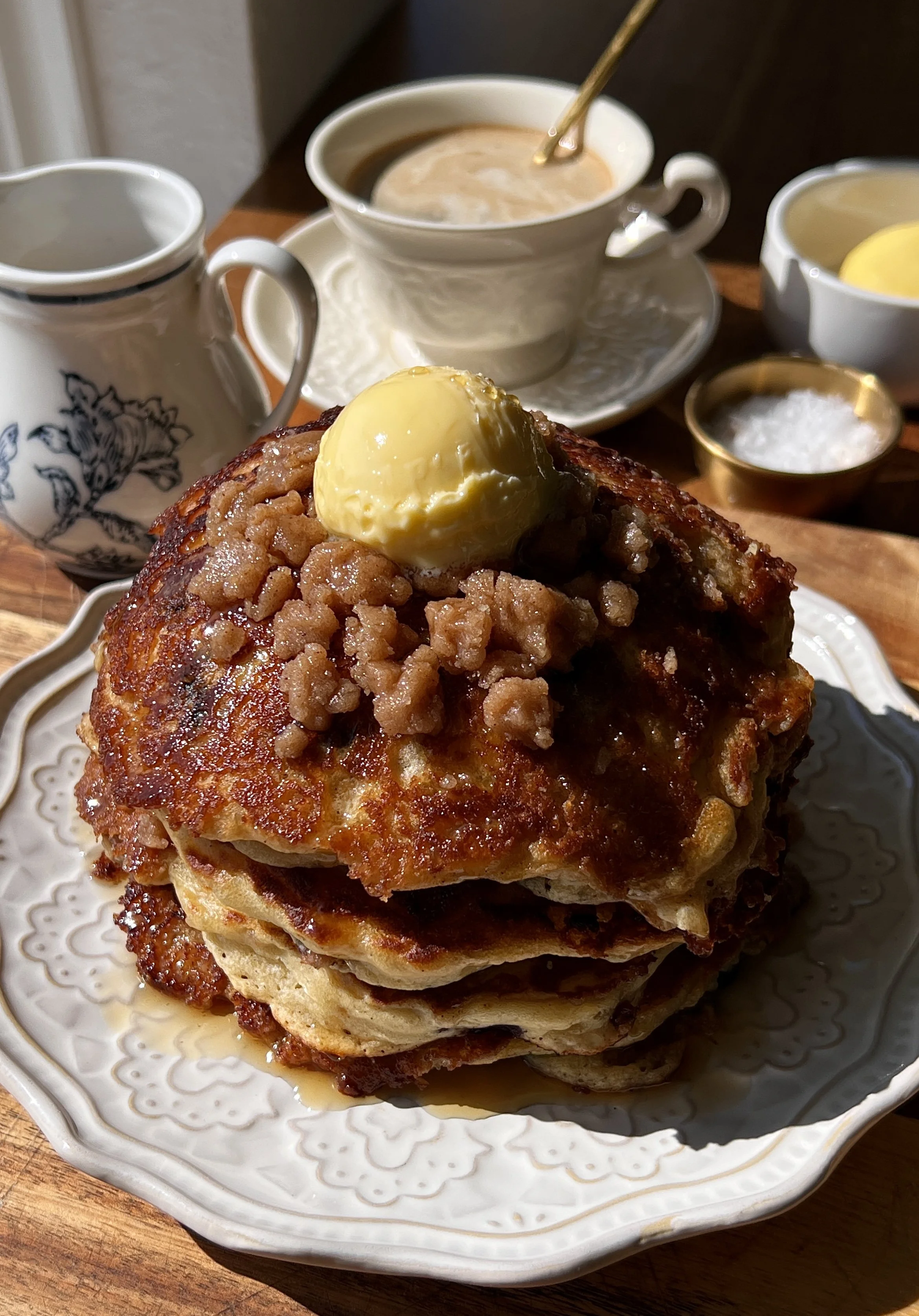 Brown butter blueberry muffin pancakes with cinnamon streusel served warm with a pat of butter, maple syrup, and a hot cup of coffee.