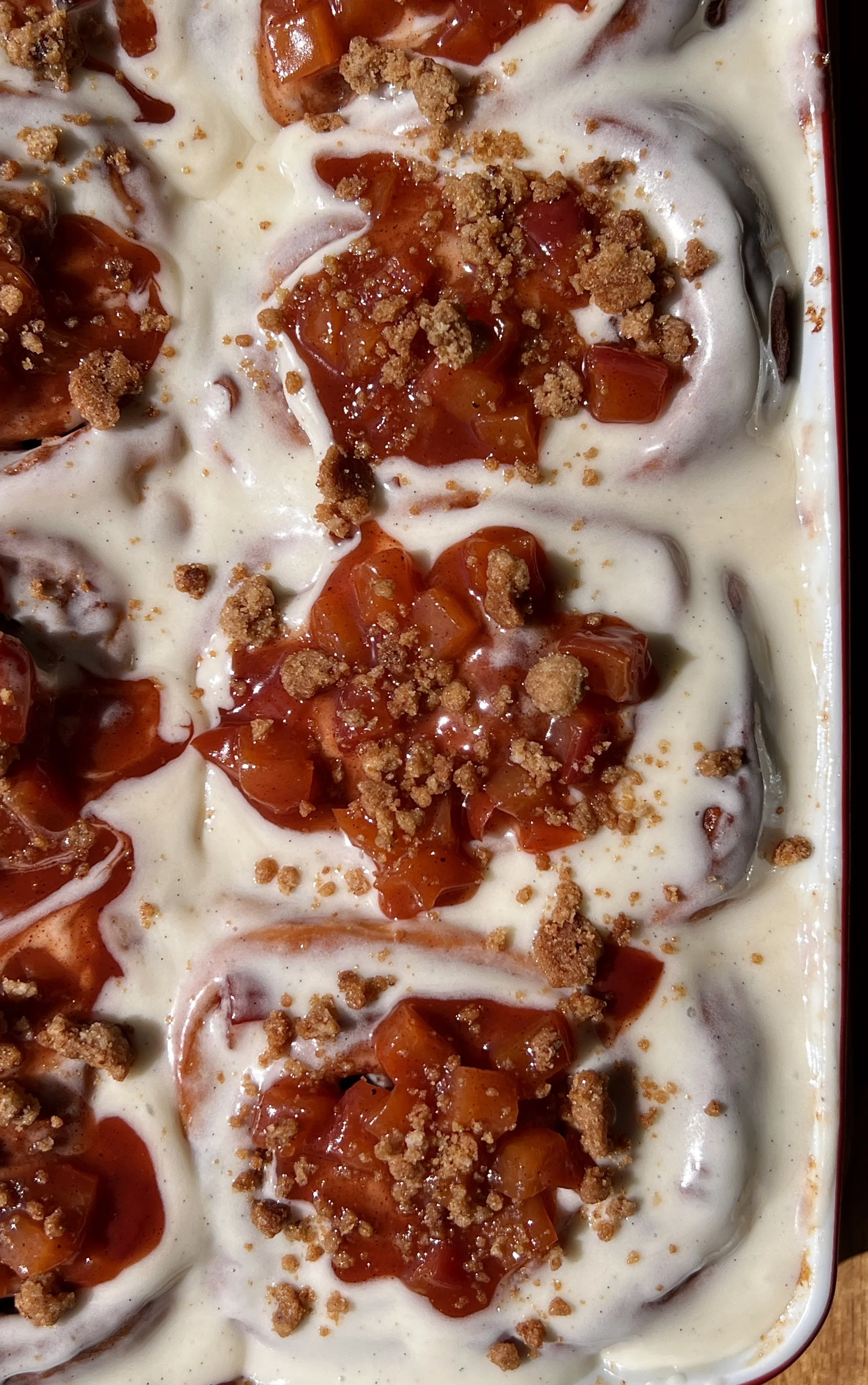 Pan of golden peach cobbler cinnamon rolls with sticky caramelized edges topped with smooth cream cheese frosting melting into every swirl.