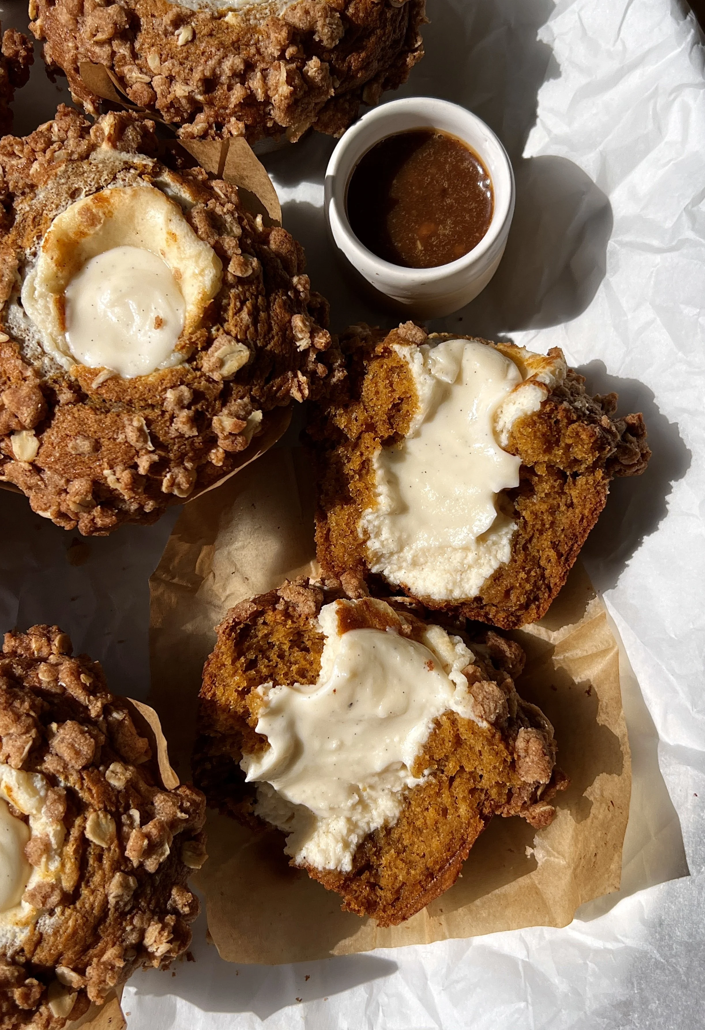 Close-up of a bakery-style pumpkin cream cheese muffin with brown butter showing the soft and fluffy delicate crumb packed with warm spiced pumpkin flavor and smooth tangy cream cheese filling with a buttery oat streusel on top.