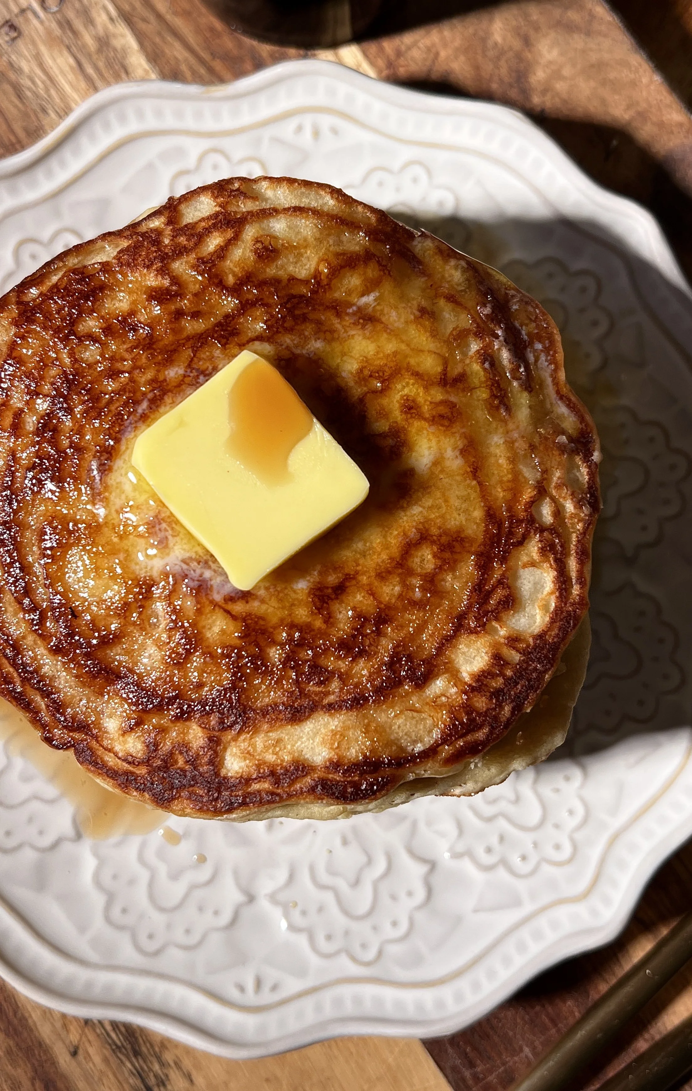 Classic buttermilk pancakes stacked high on a plate, soft and fluffy with golden edges, topped with butter and maple syrup, served alongside a warm maple brown butter latte.