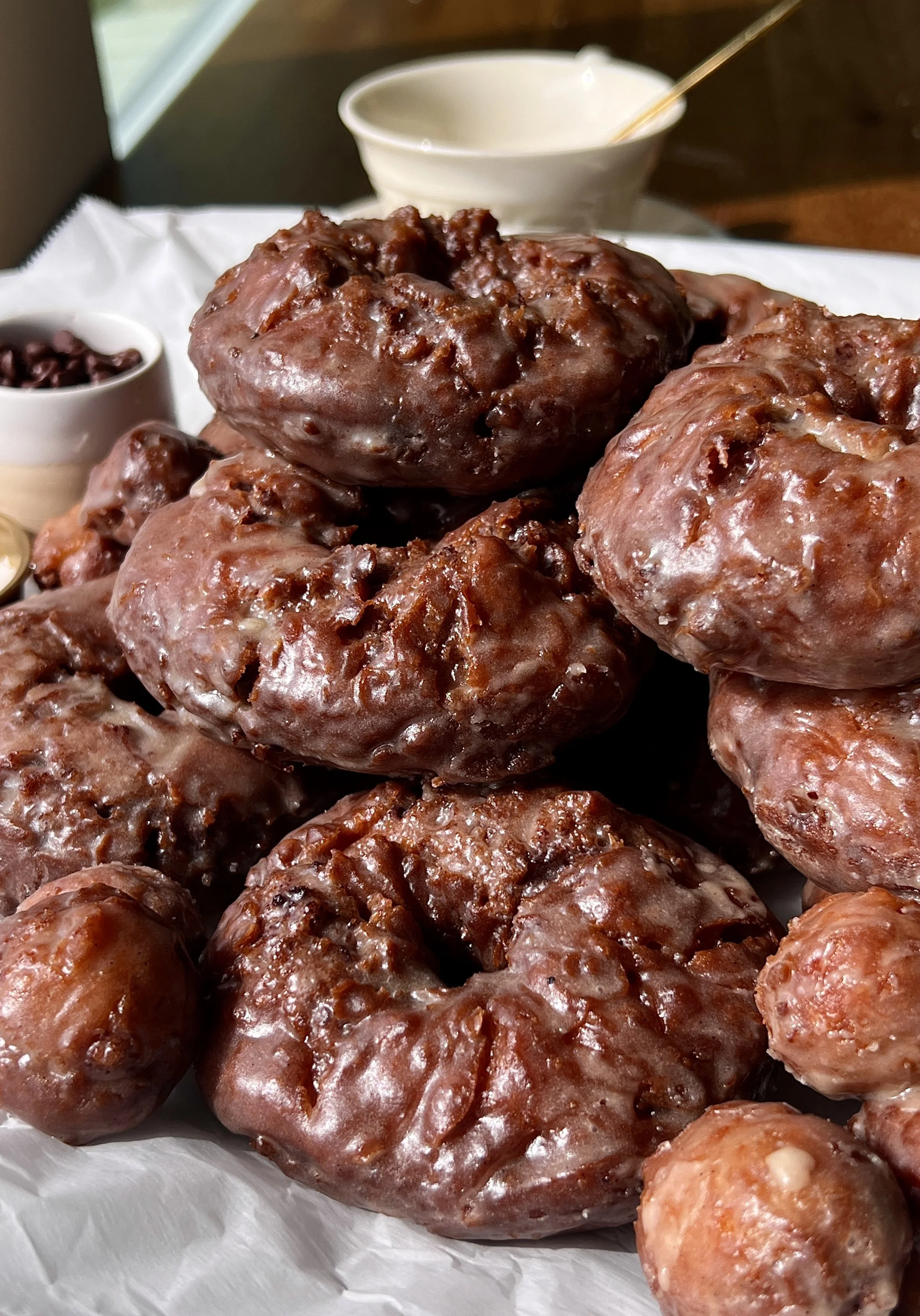 Stack of golden old-fashioned chocolate chip banana bread donuts coated in salted brown butter honey glaze served with a hot cup of coffee.