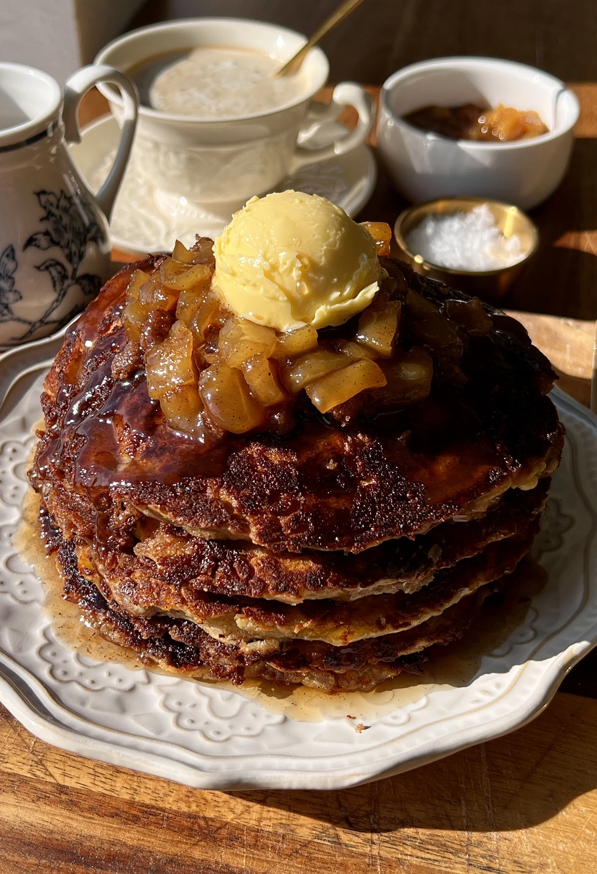 Apple streusel griddle cakes with a golden exterior and crisp edges with warm gooey apple filling and caramelized cinnamon streusel served warm with a pat of butter, maple syrup, and a hot cup of coffee.