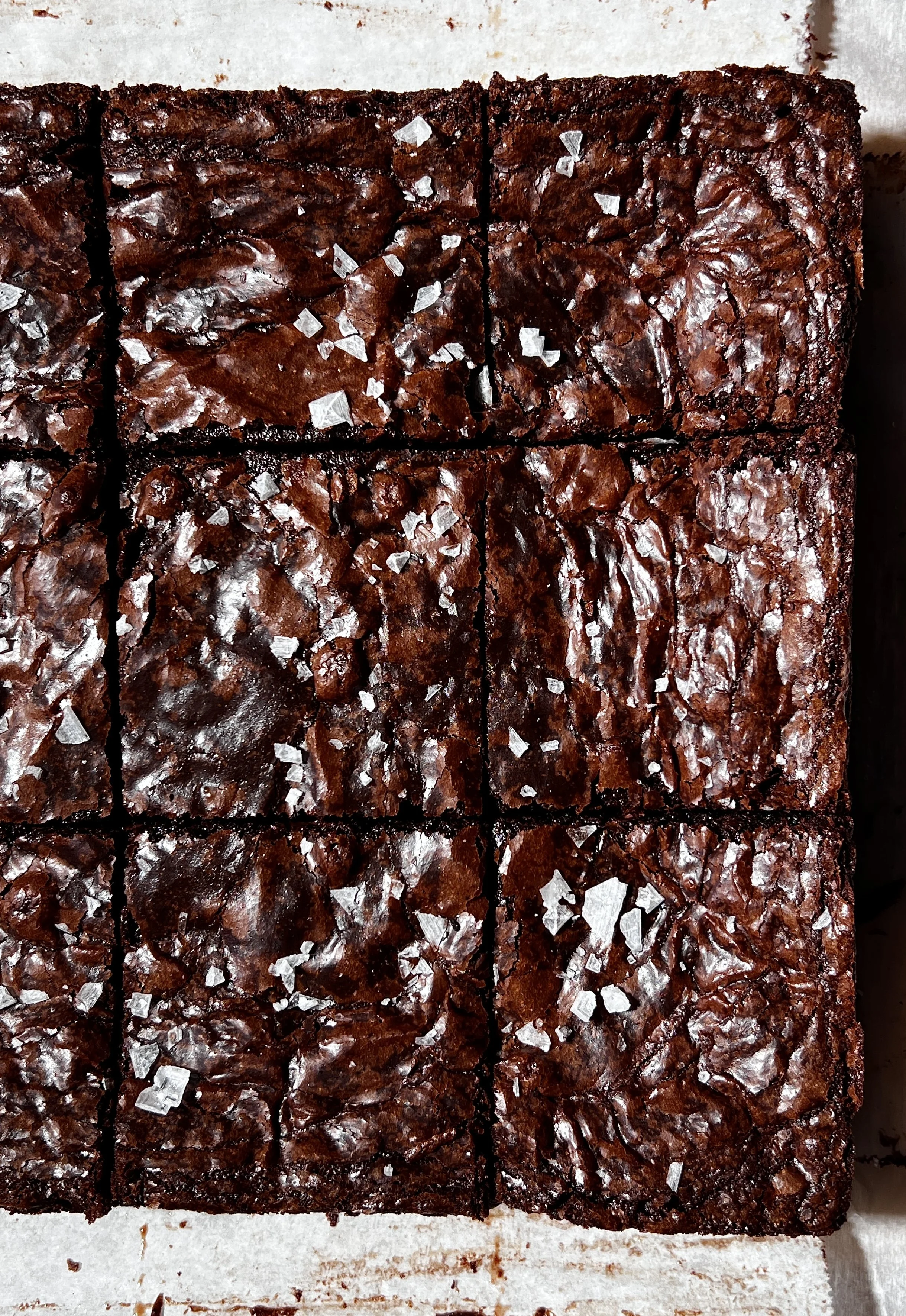 Close-up of fudgy crinkle-top brown butter brownies showing a shiny crackled surface and melty chocolate chips.