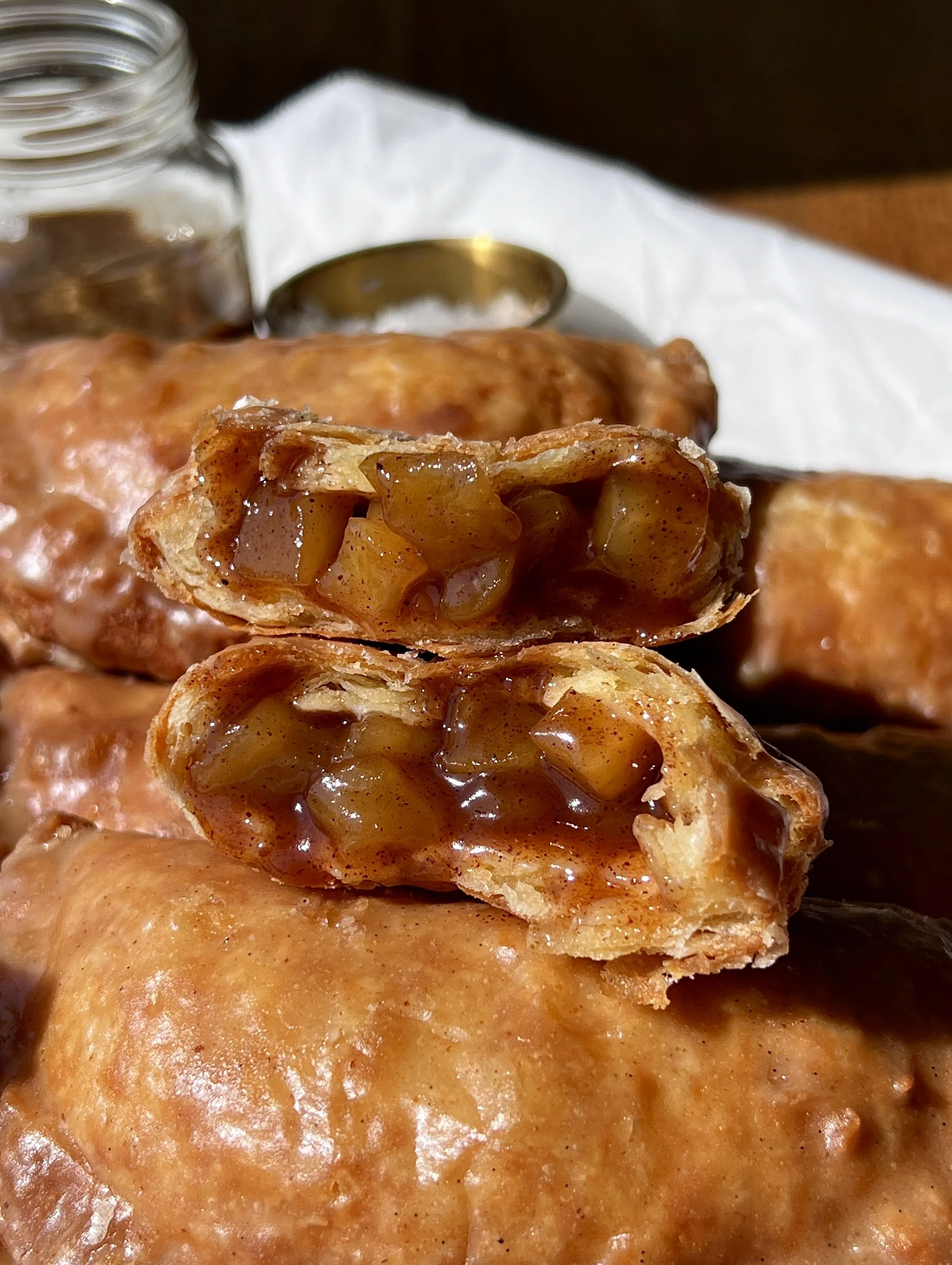 Close-up of a golden fried apple hand pie with a flaky buttery crust and warm and gooey spiced apple pie filling throughout finished with a brown butter maple vanilla bean glaze.