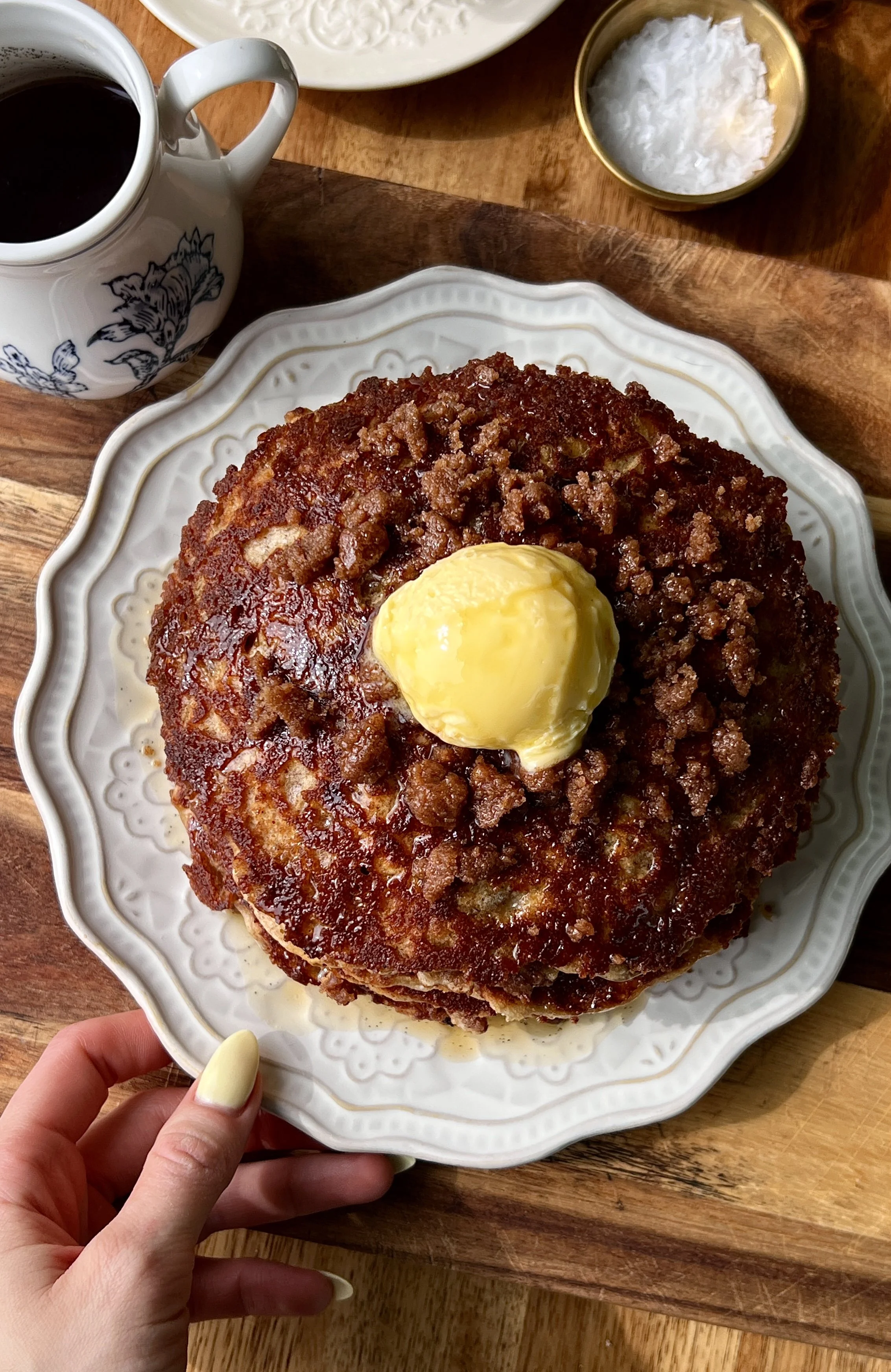 Soft and fluffy banana coffee cake pancakes with a perfectly golden exterior and caramelized cinnamon streusel throughout served warm with a pat of butter, a drizzle of warm vanilla bourbon maple syrup, and a hot cup of coffee.