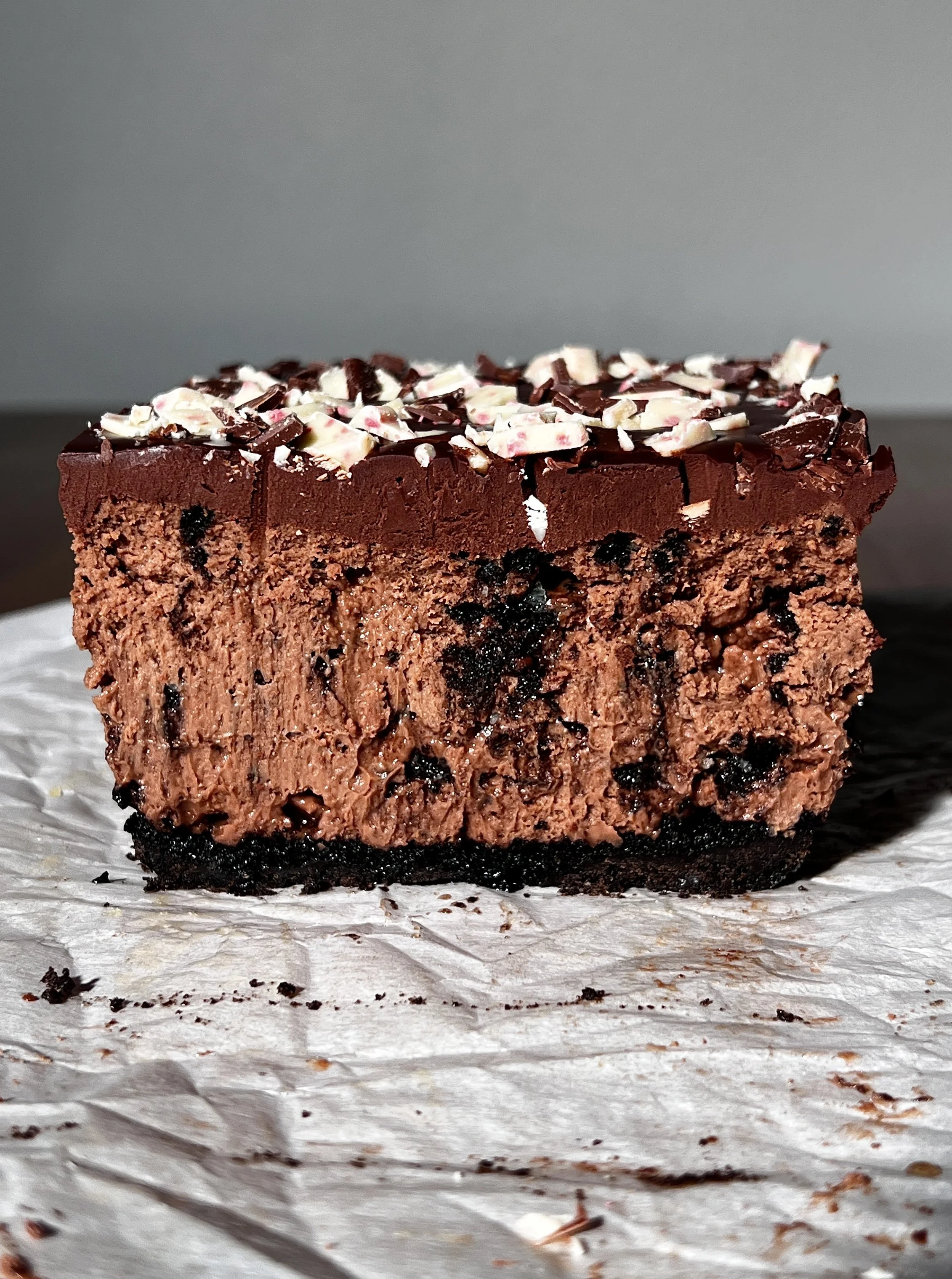Close-up of peppermint Oreo cheesecake bars with a dark Oreo crust, creamy peppermint mocha cheesecake filling, chocolate ganache topping, and chopped peppermint bark sprinkled on top.