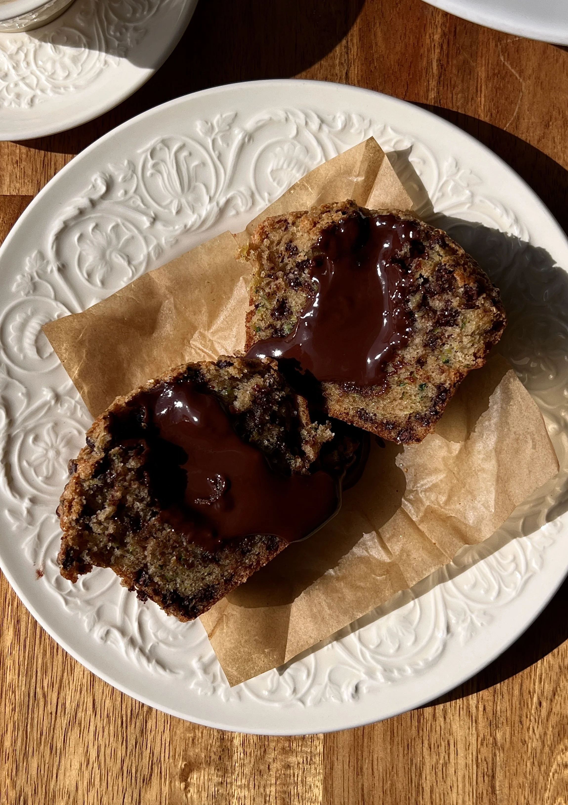Soft and fluffy bakery-style chocolate fudge zucchini muffins with a tall beautifully golden muffin top, melty chocolate chips throughout, and a warm molten chocolate ganache center served warm with a hot cup of coffee.