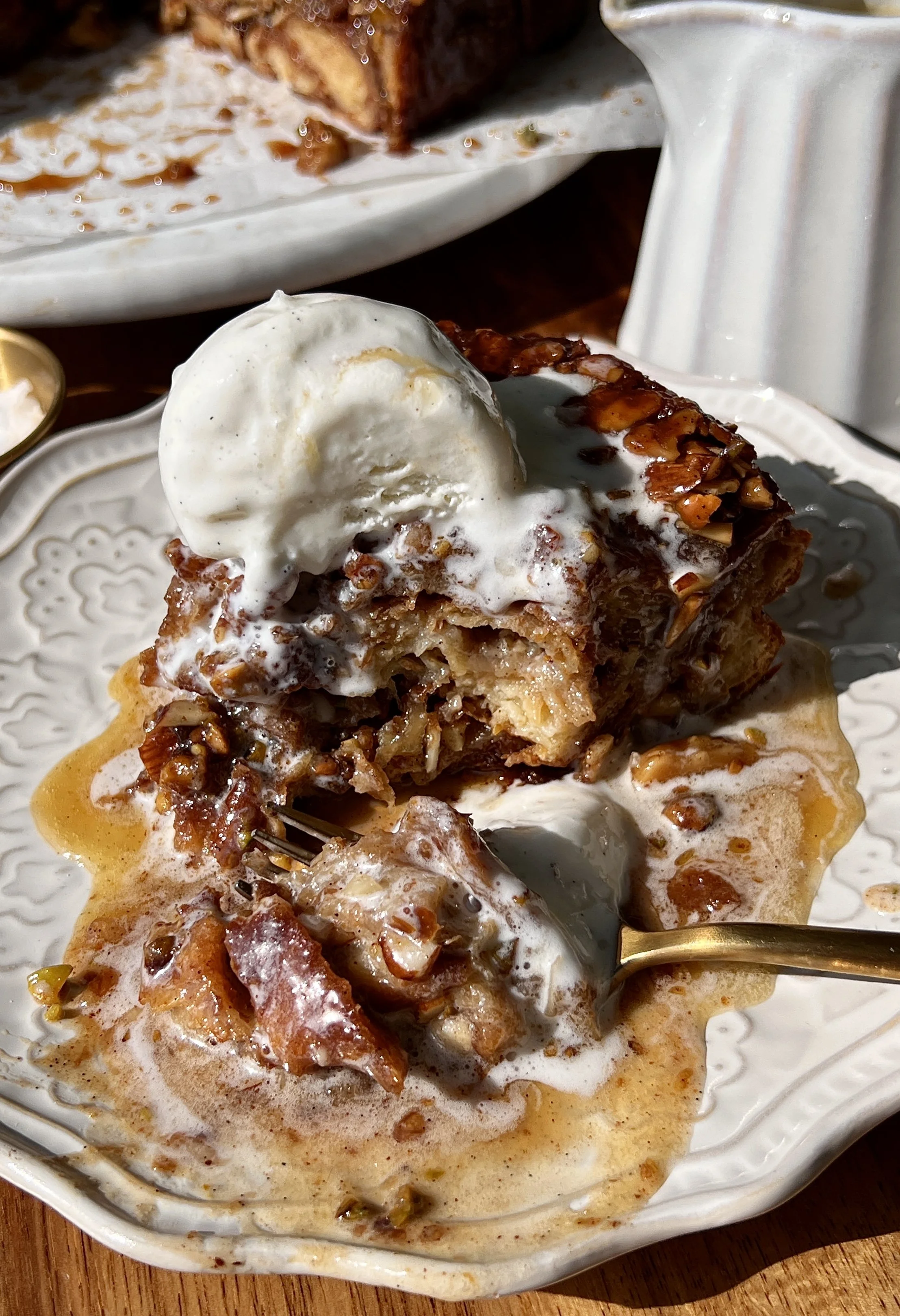 Golden baklava croissant bread pudding made with buttery flaky croissants and vanilla bean custard swirled with a warm gooey baklava filling served warm with a scoop of vanilla ice cream, honey buttermilk syrup, and flaky sea salt.