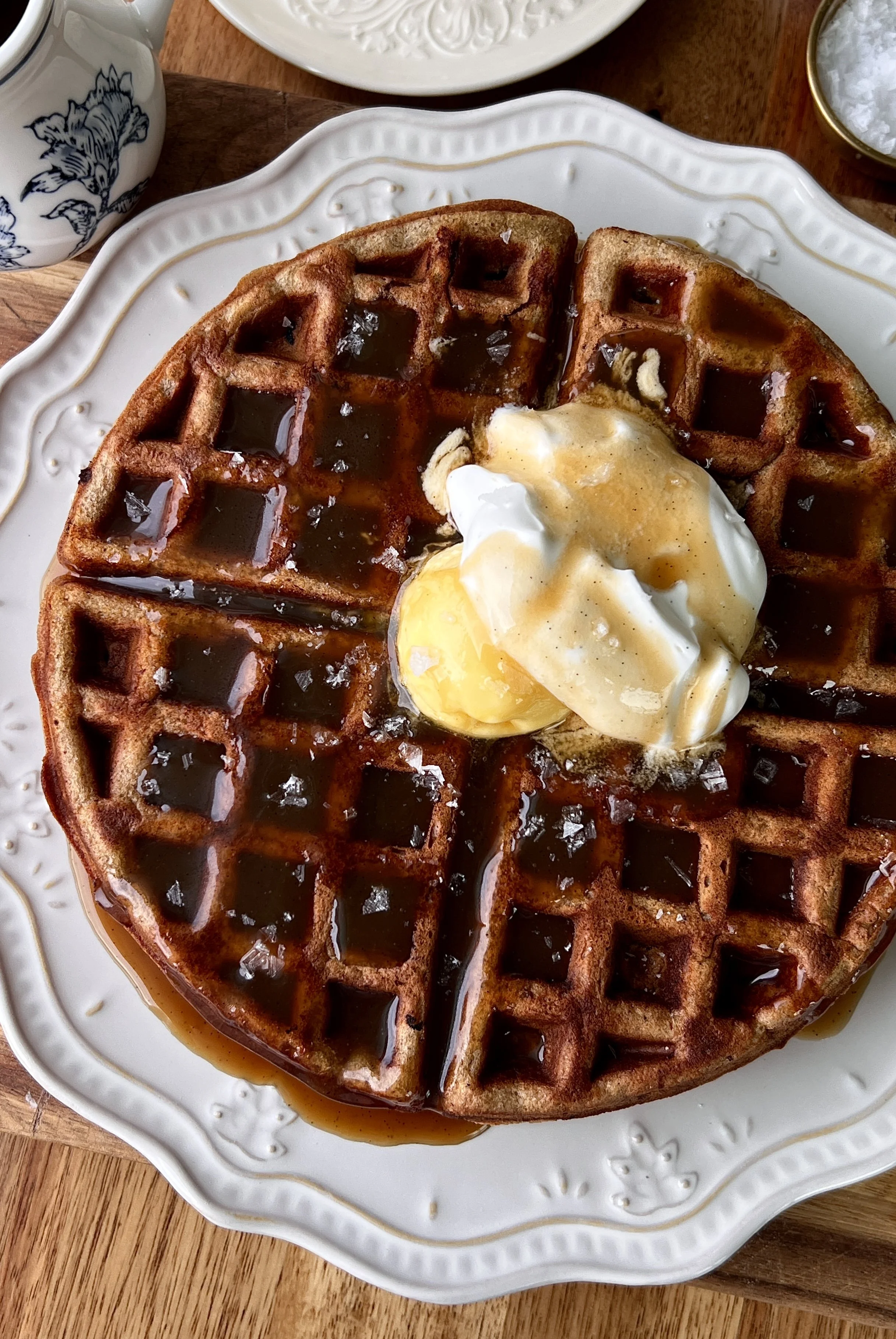 Sticky toffee waffles served warm with butter, whipped sour cream topping, and a drizzle of silky maple toffee sauce with a hot cup of coffee.
